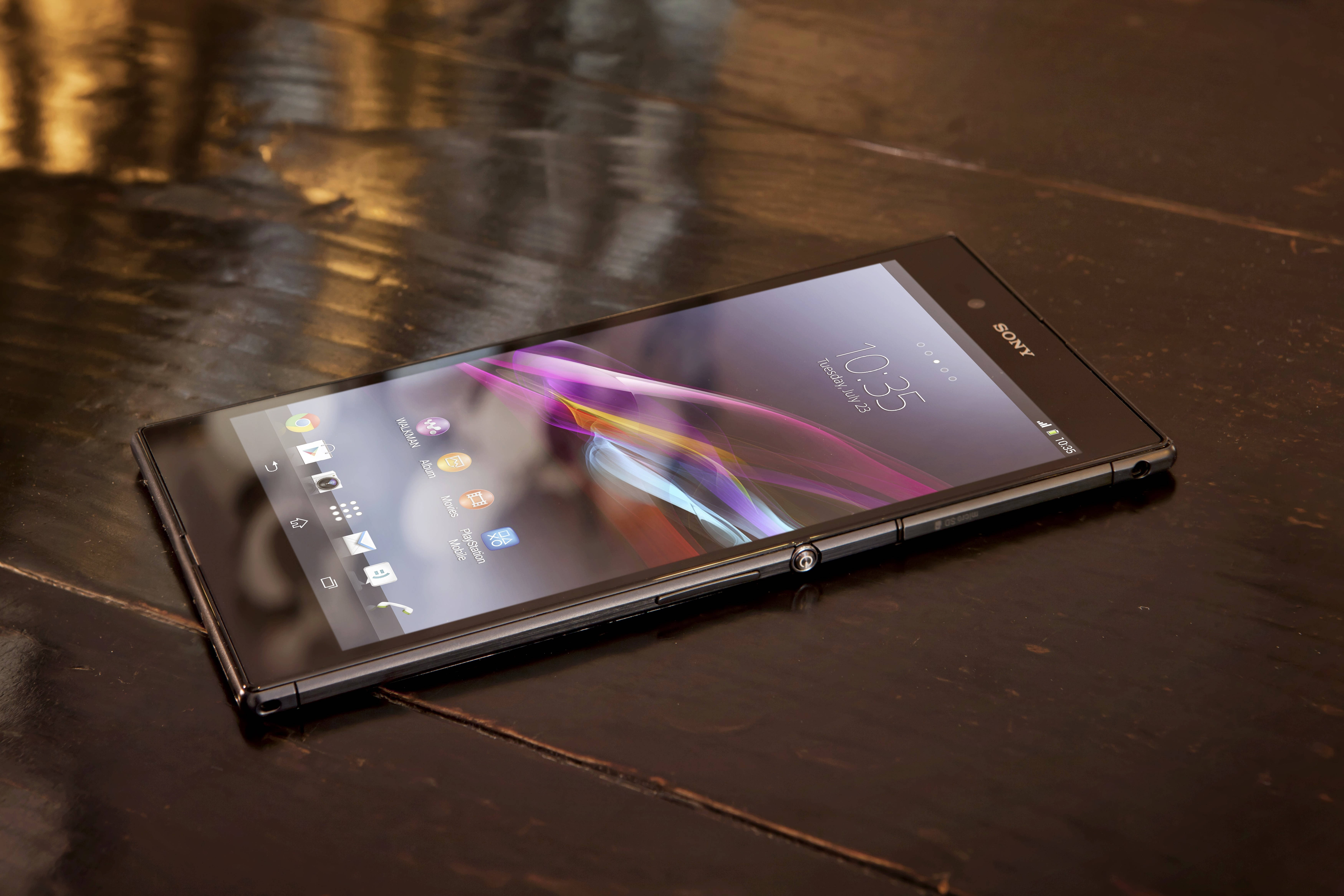 索尼Xperia Z 壁紙 — 一部時尚的黑色Sony智能手機，帶有彩色抽象桌布，對角放置在深色木質表面上。