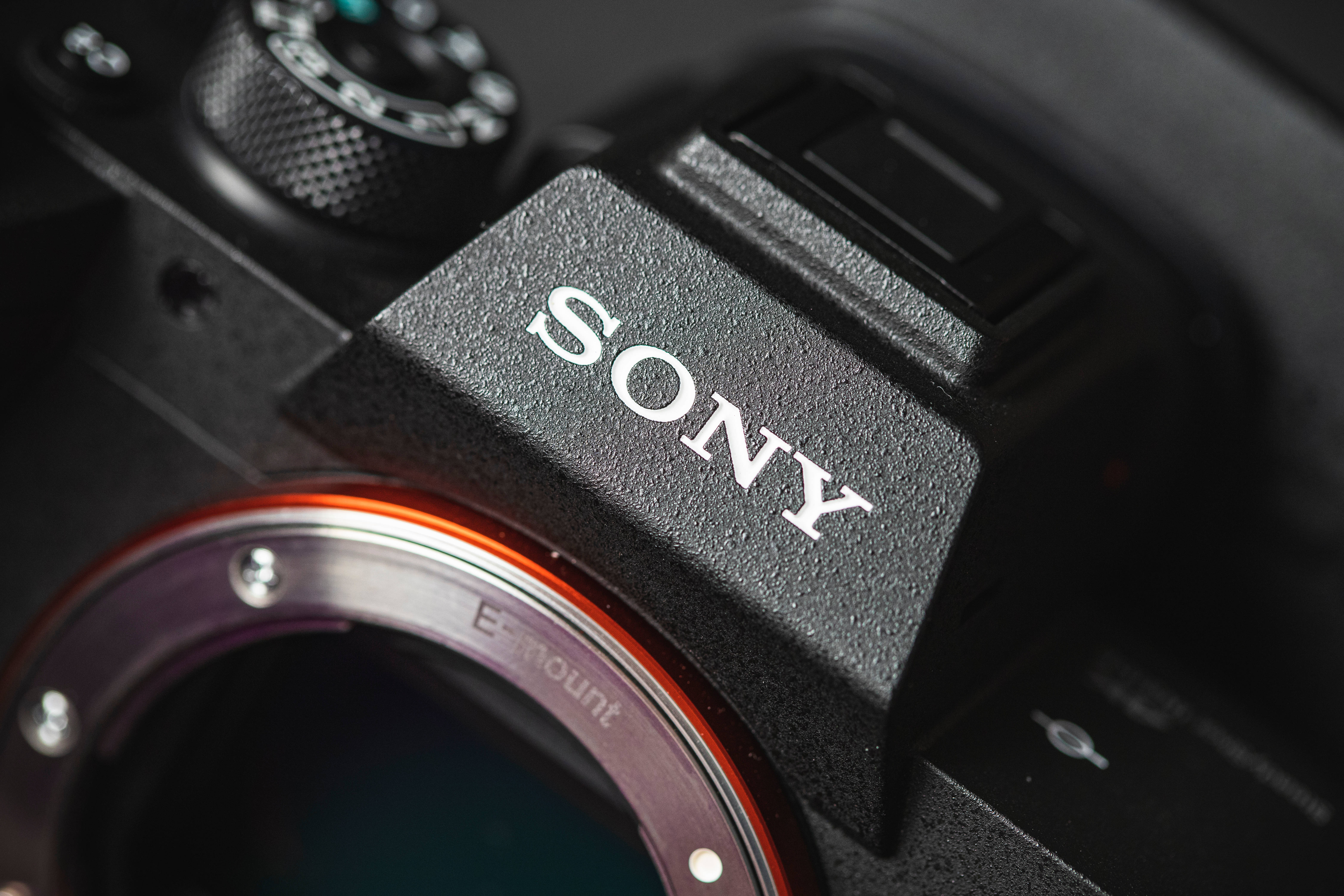 索尼單眼相機特寫 壁紙 — 黑色Sony相機機身特寫，顯示品牌標誌和帶有橙色裝飾環的鏡頭接環。