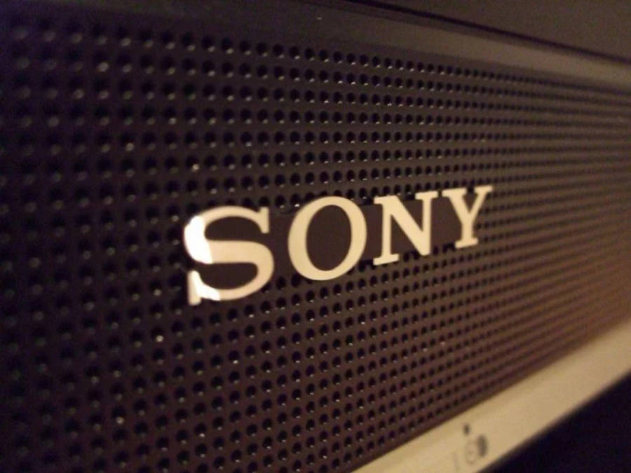 索尼標誌實物設備特寫 壁紙 — Sony 喇叭格柵的特寫，金屬標誌在溫暖的環境光下發光。