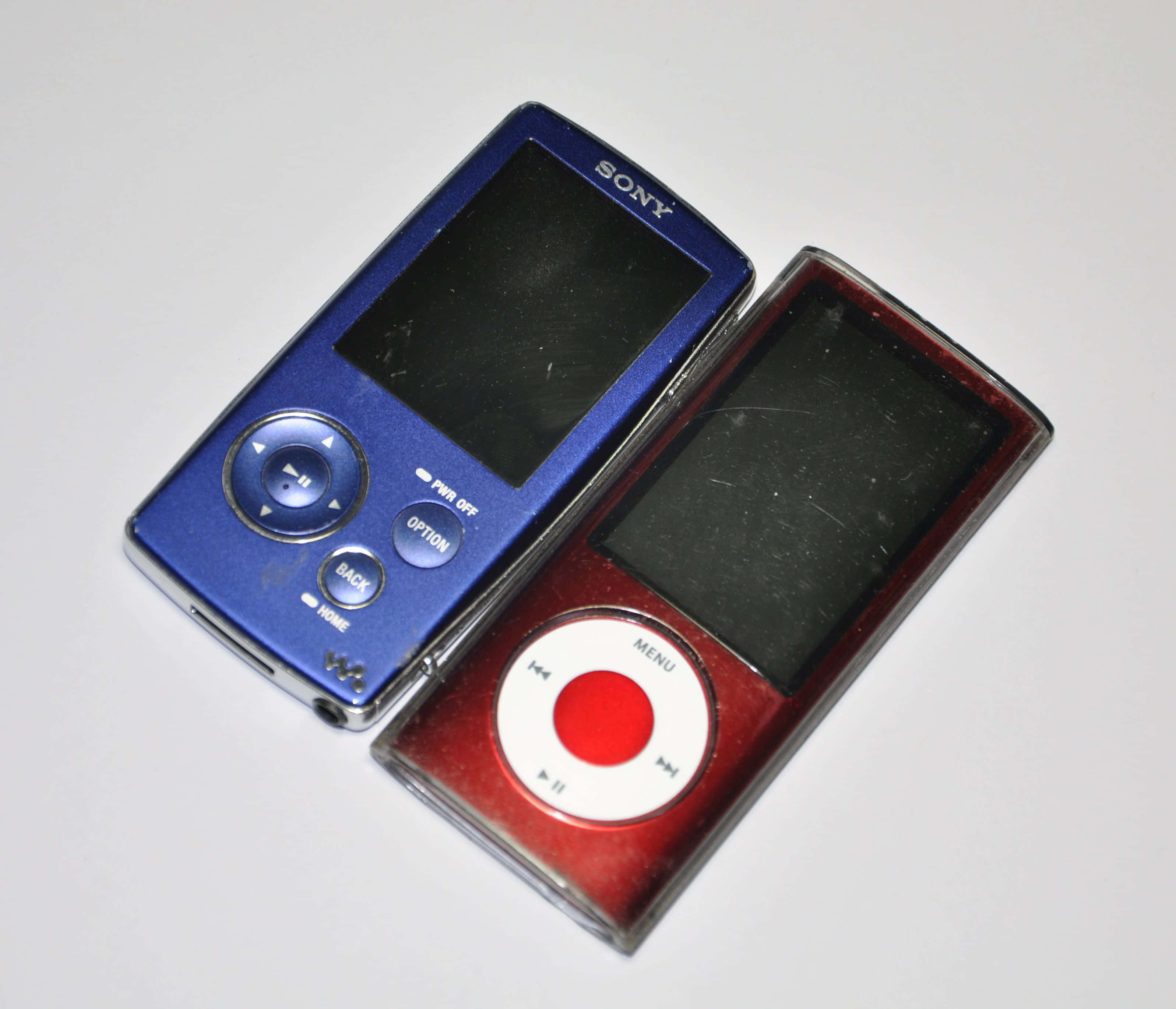 索尼與iPod MP3圖片 壁紙 — 兩部復古便攜式音樂播放器，藍色Sony Walkman和紅色Apple iPod Classic，並排放在白色平面上。