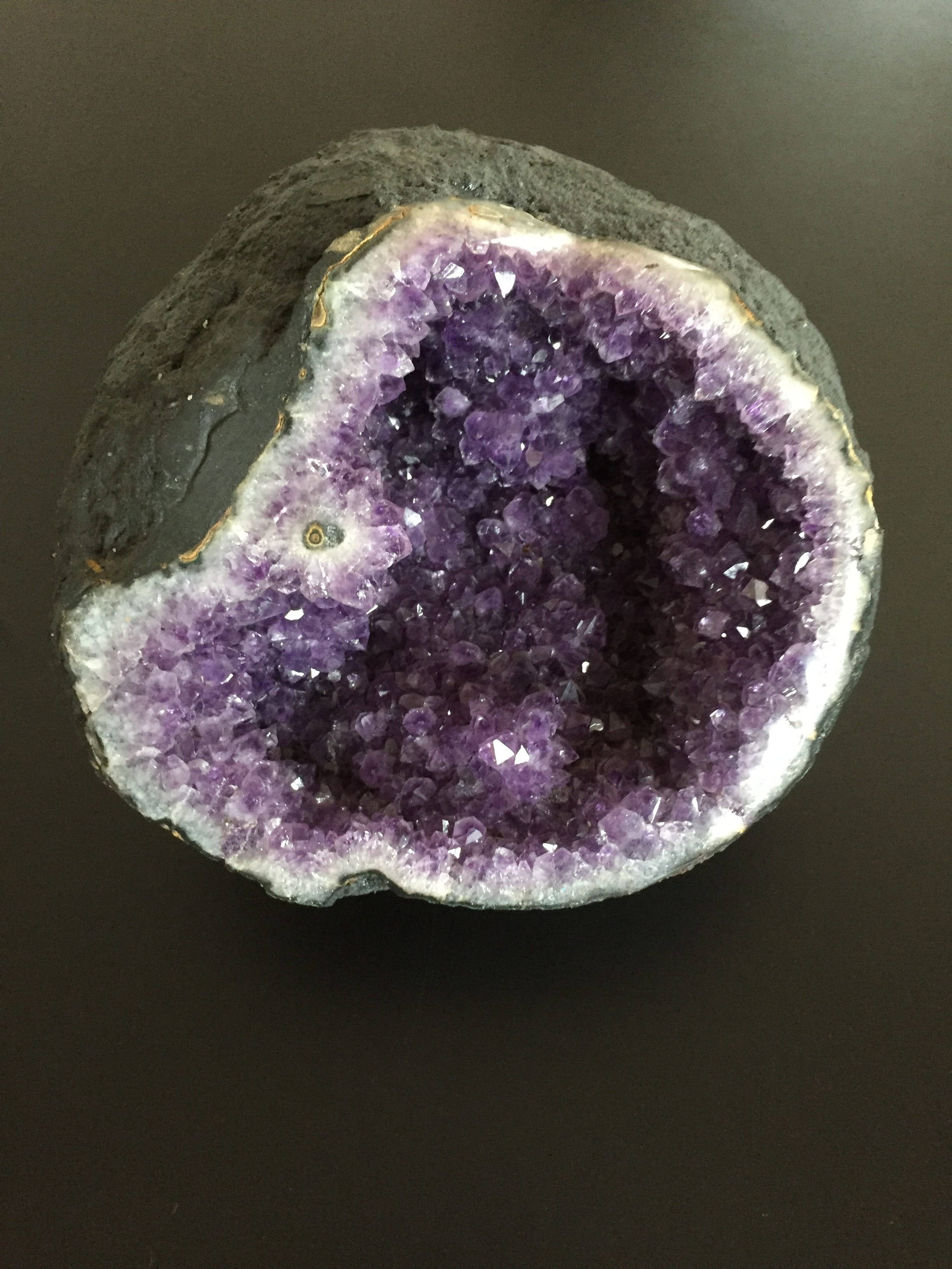 紫水晶晶洞與白agate 壁紙 — 一塊切割的紫水晶晶洞在黑色表面上展現出閃閃發光的紫色晶體，外部為深灰色。