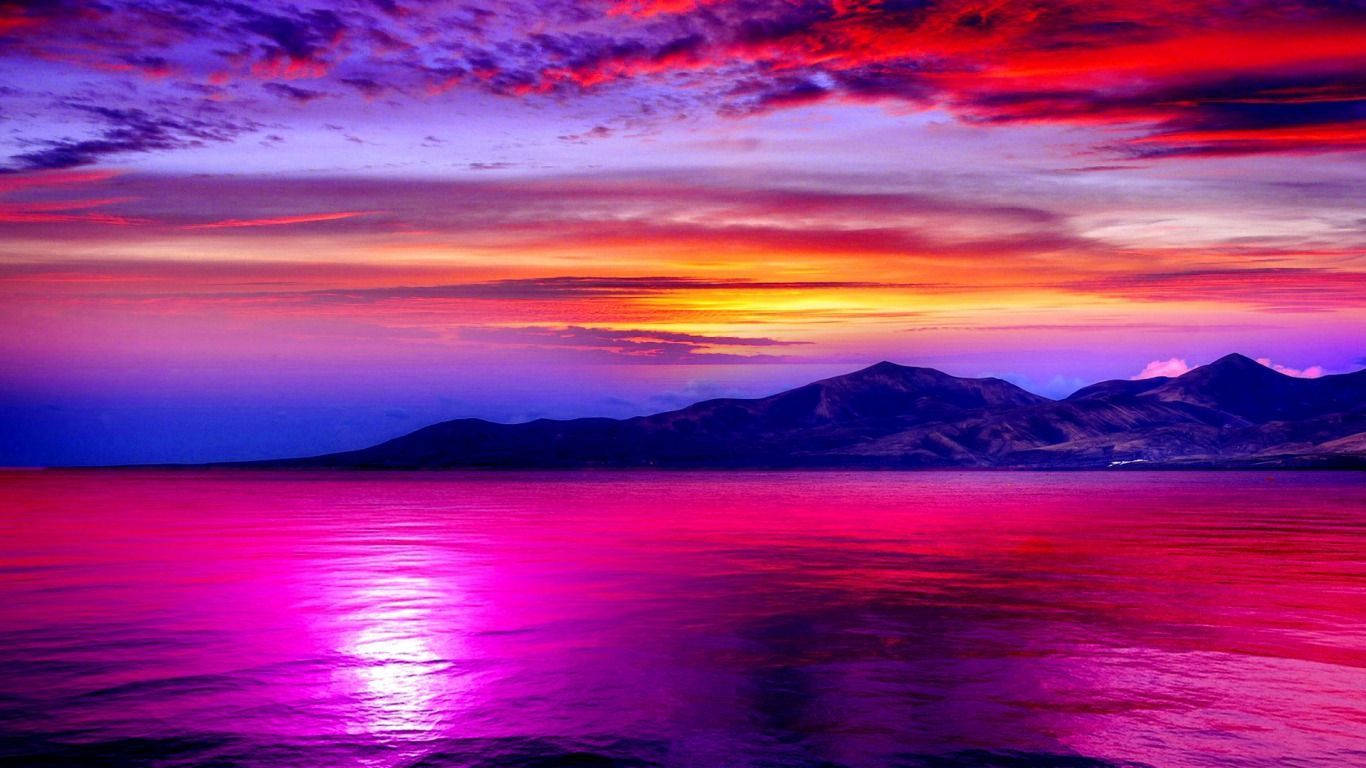 鮮豔的粉紅色和紫色夕陽映照在平靜的水面上，遠處有山巒。