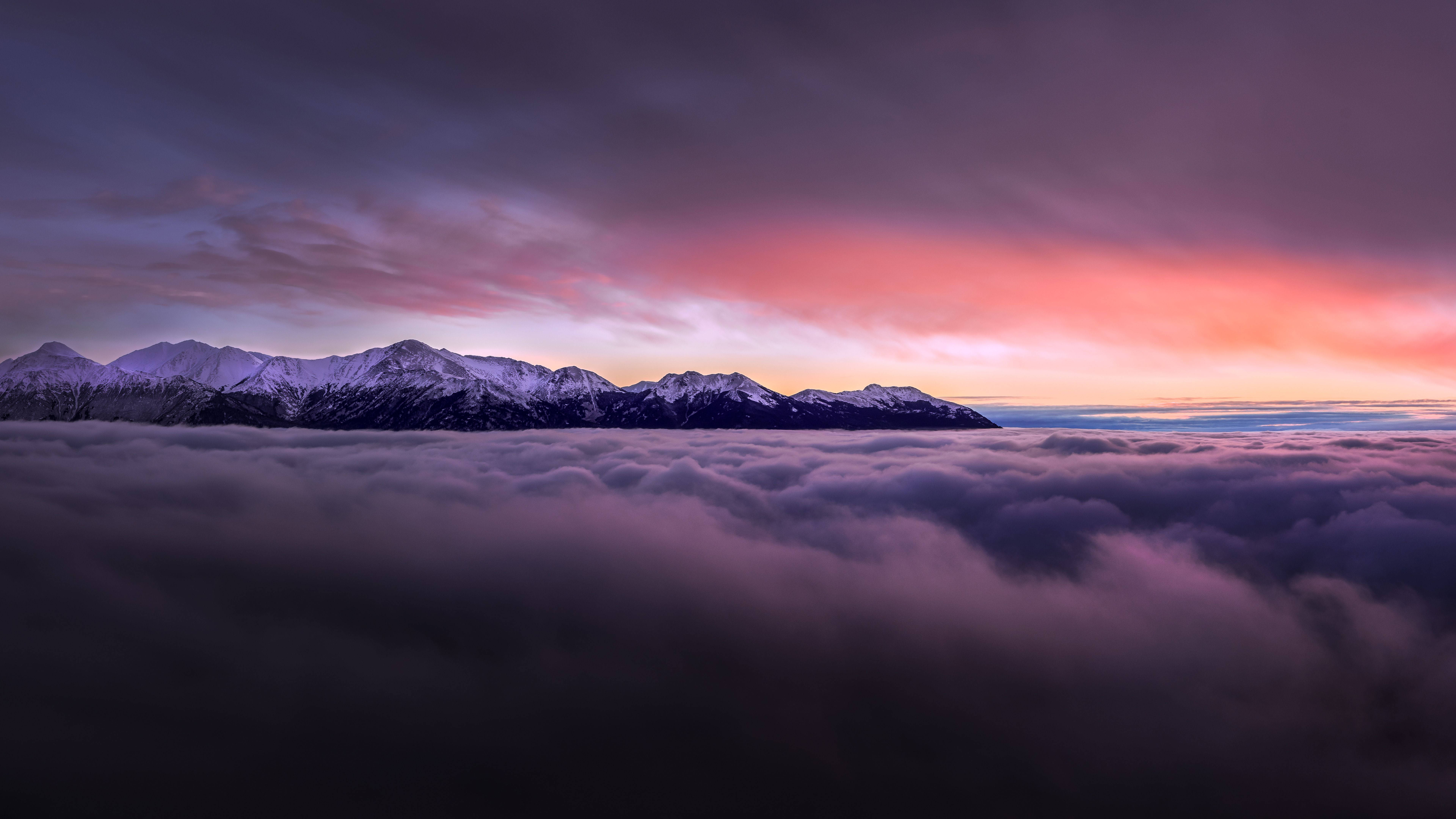 紫白雲朵對比的天空美景 壁紙 — 白雪覆蓋的山峰在充滿活力的粉紅色和紫色日落天空下，聳立於雲海之上。