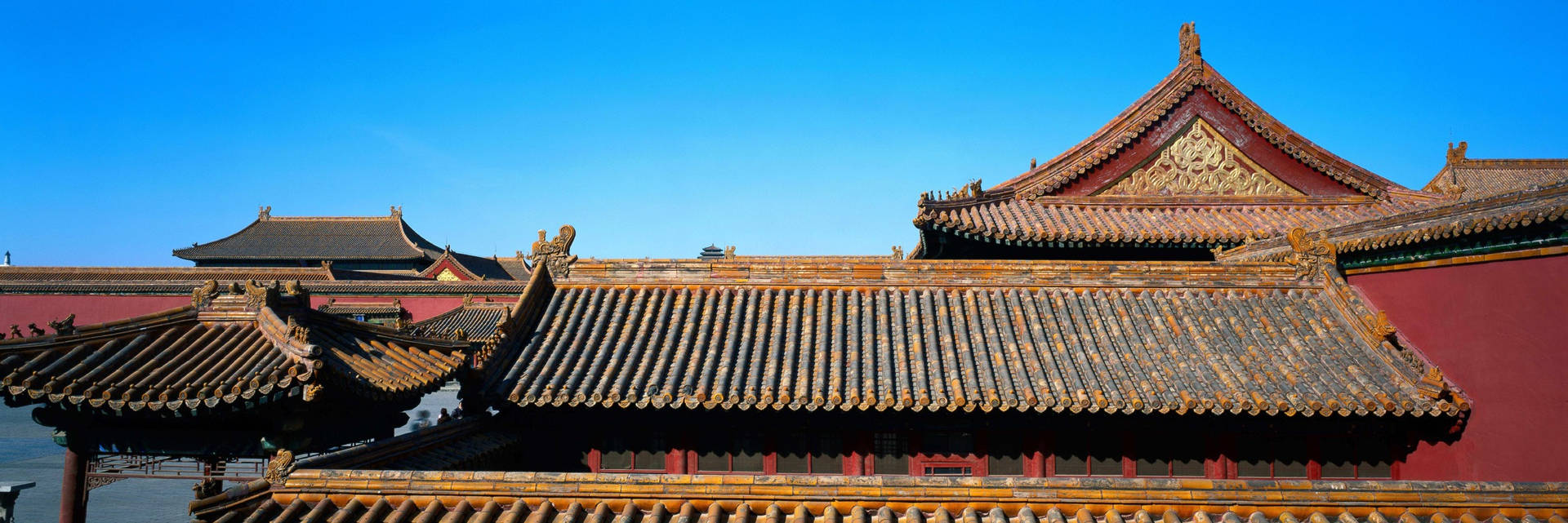 古代中國宮殿屋頂，帶有金色細節和灰色瓦片，在明亮藍天下。