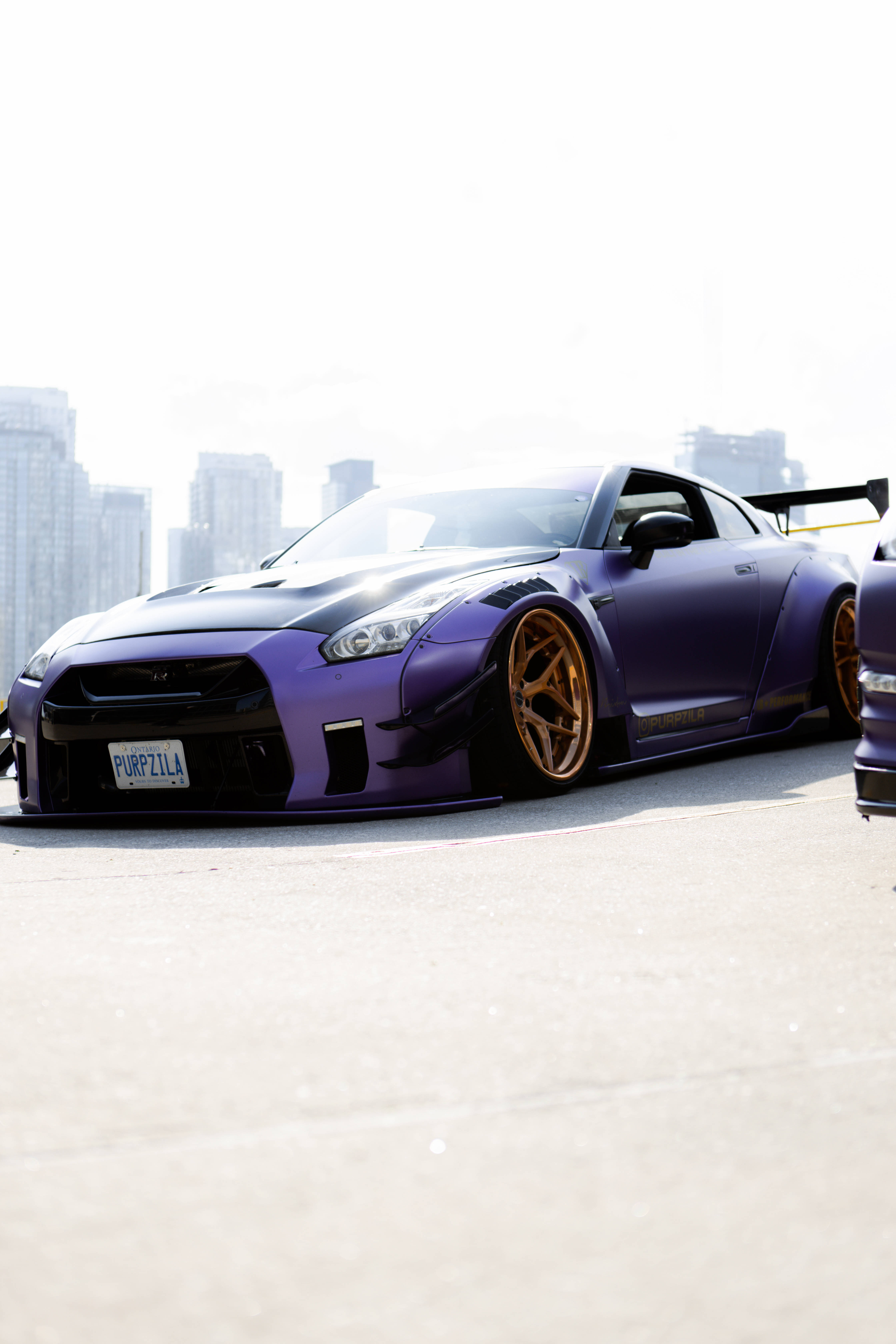 紫色Nissan Skyline GTR R34 壁紙 — 一輛啞光紫色的日產GT-R配金色輪圈，停泊在城市天台，背景是朦朧的天際線。