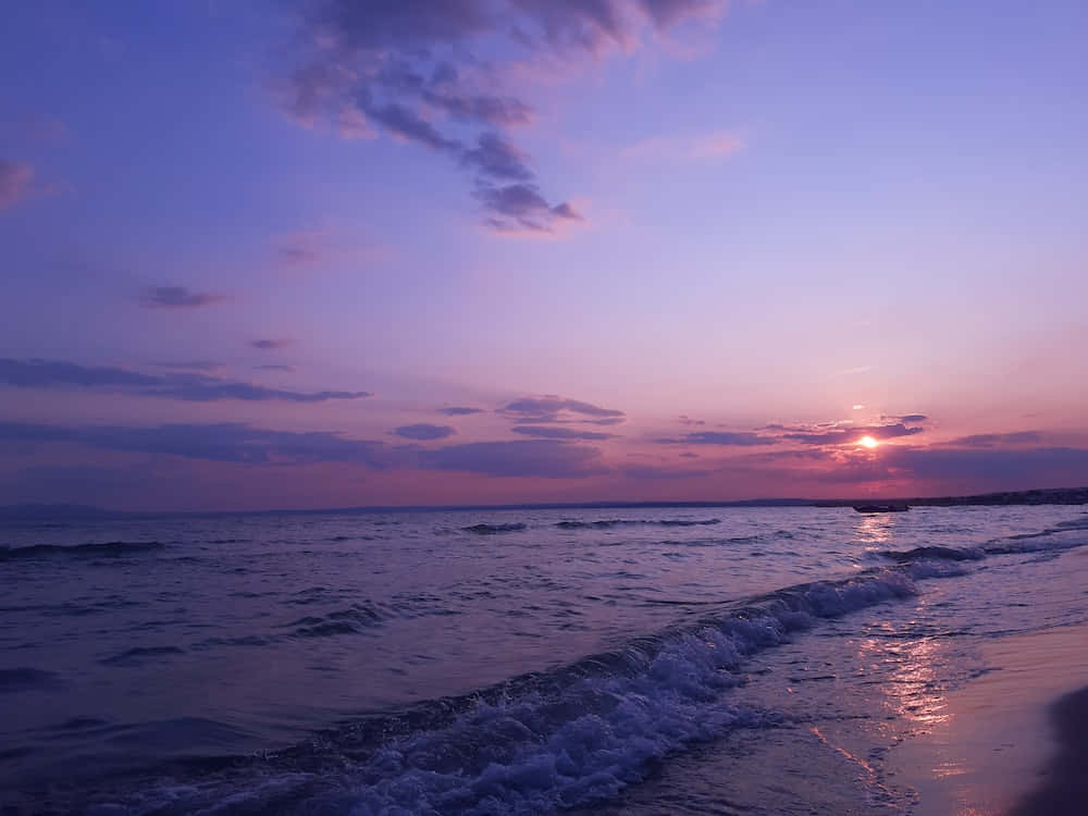 紫色夕陽映照海面的美學圖 壁紙 — 日落時分寧靜的海灘，紫色和粉紅色的天空倒映在輕柔的海浪上，拍打著濕沙。
