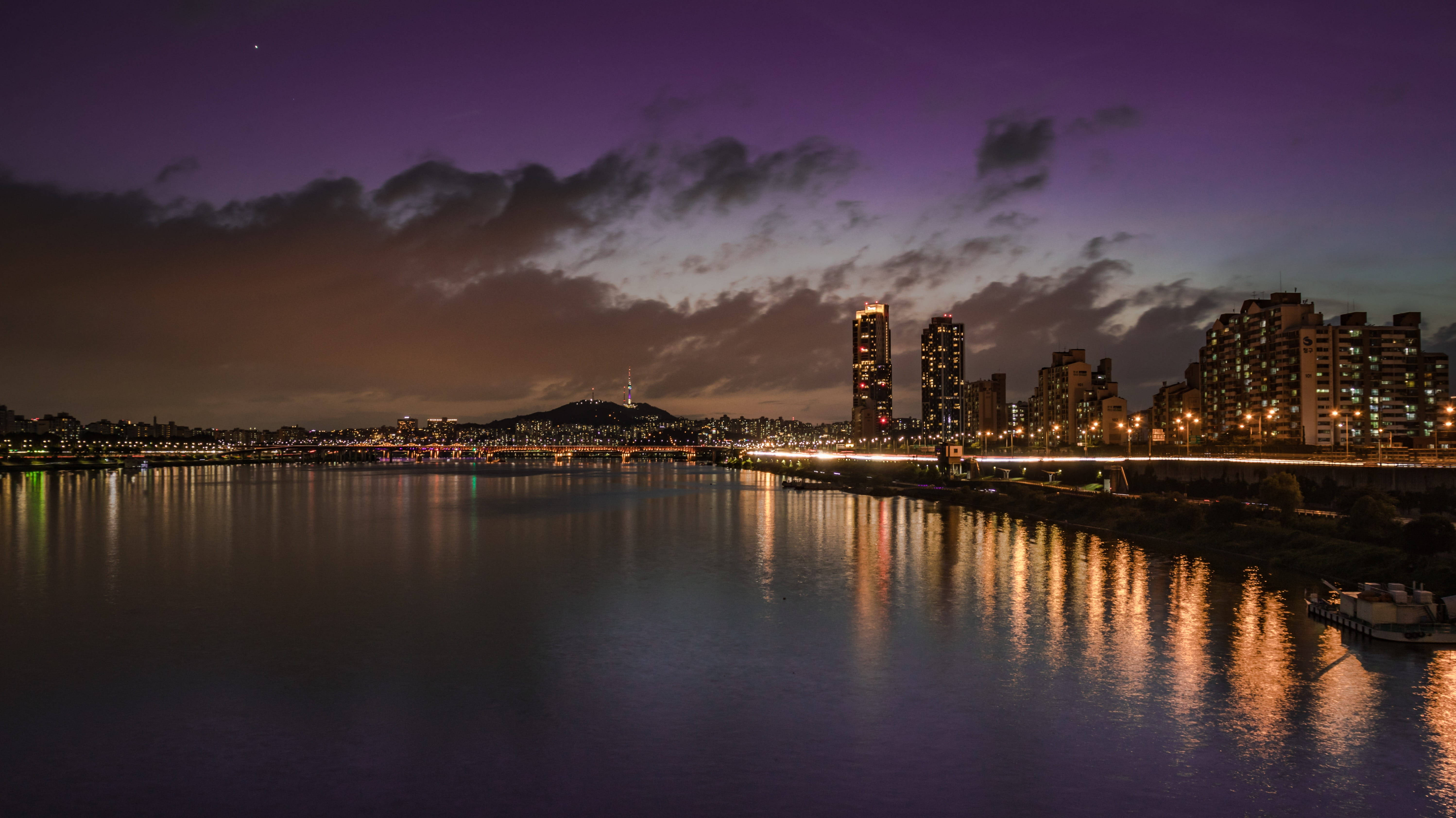 紫色夜空河景 壁紙 — 城市天際線在黃昏時分，發光的燈光映照在平靜的河面上，天空呈現紫色。