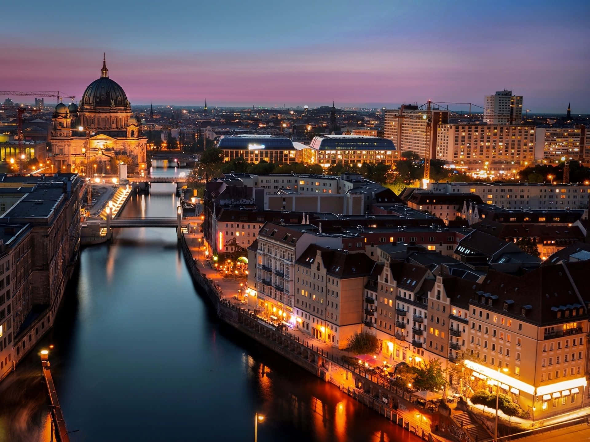 Germany 桌布 壁紙 — 紫色天空下，河流倒映建築物和圓頂大教堂溫暖燈光的暮色城市景觀。