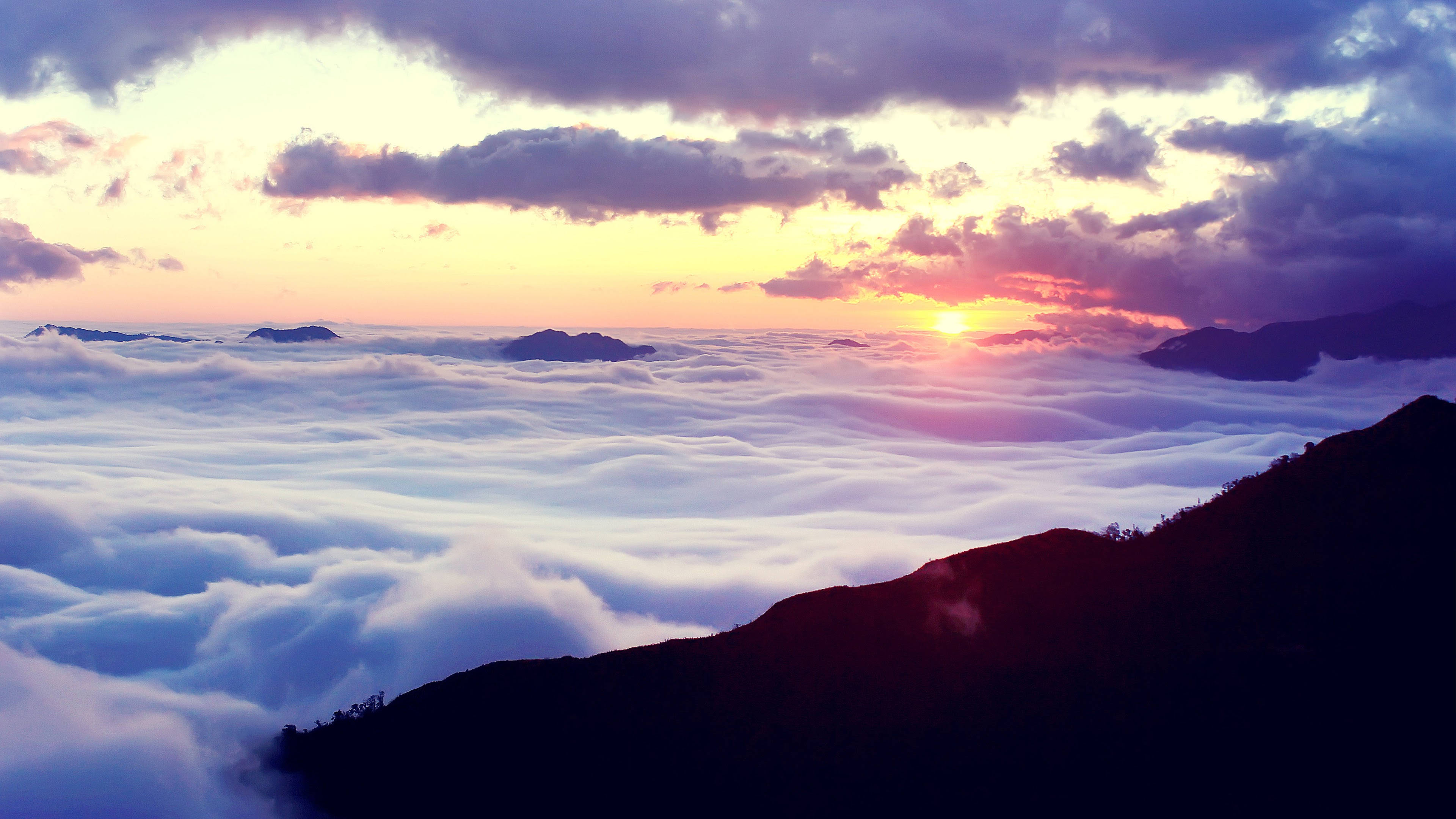 紫色天空與日落的寧靜風景 壁紙 — 夕陽將雲彩染成火熱的橙色和紫色，山脈在雲海之上聳立。