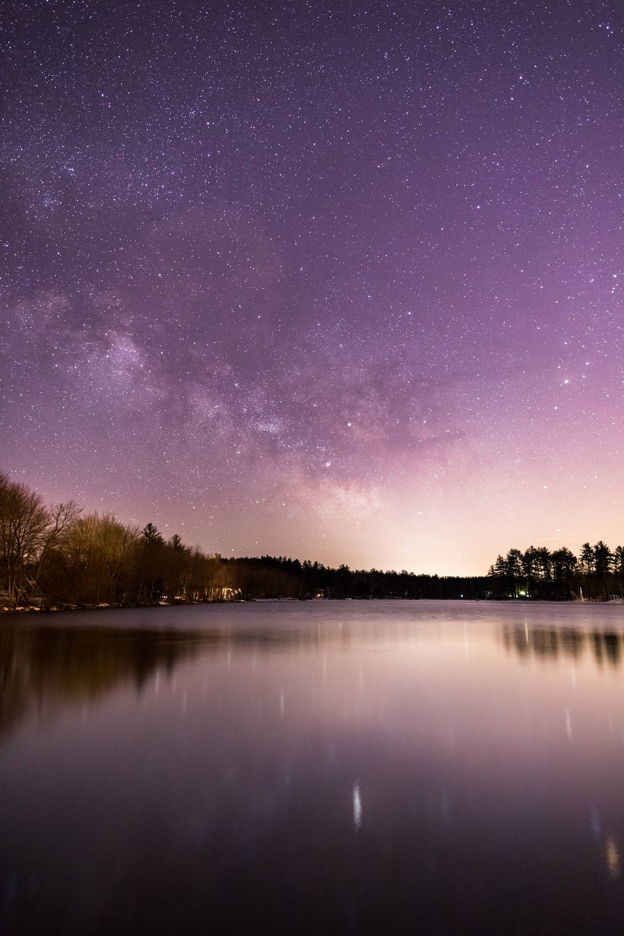 結冰的湖面反射出帶有銀河和森林剪影的星空紫色夜空。