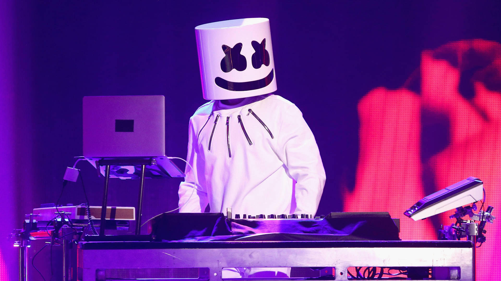 DJ Marshmello 在音樂會上表演，伴隨著發光的紫色燈光和設備。