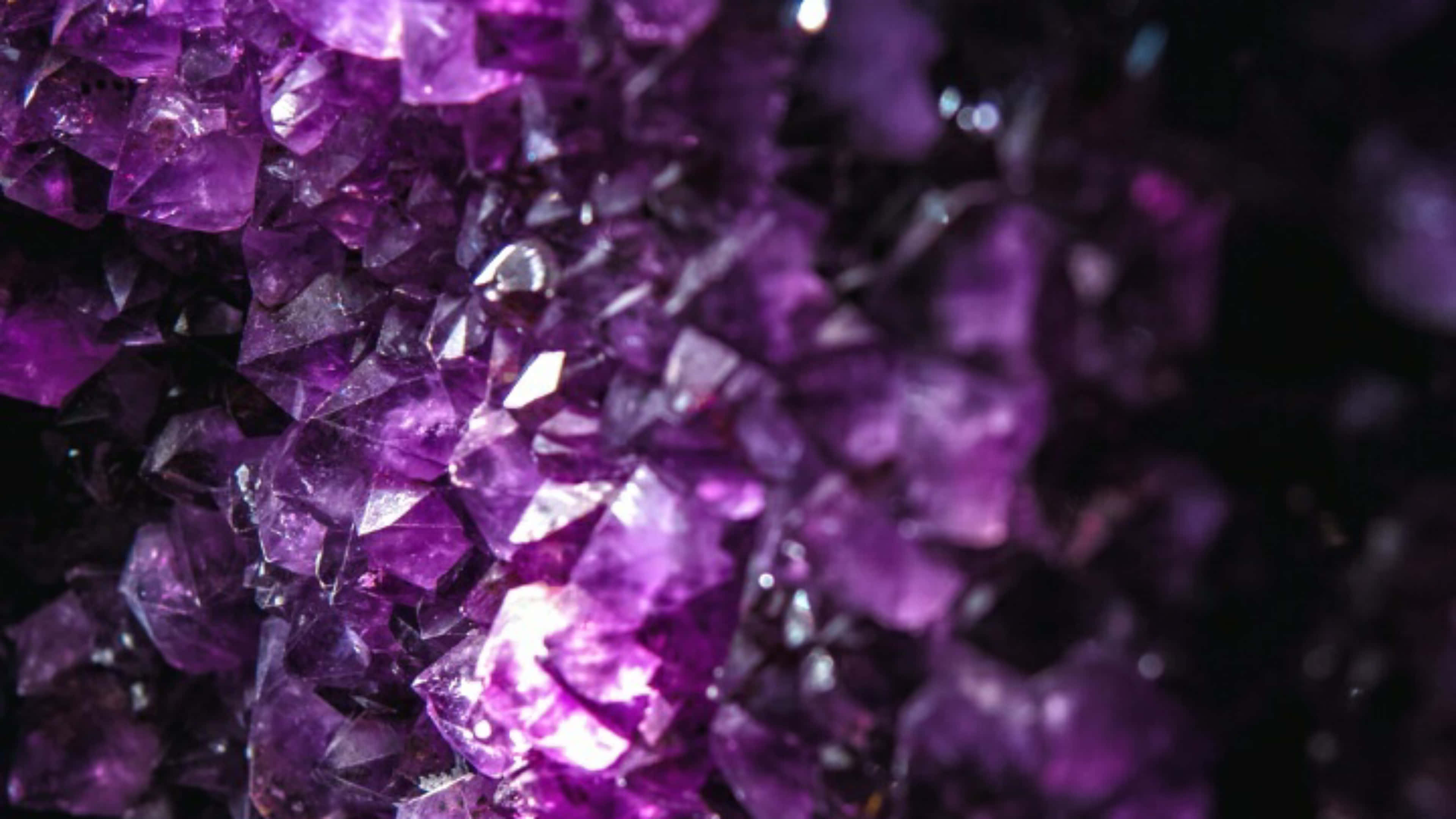Amethyst 桌布 壁紙 — 紫色閃亮紫水晶晶體的近距離特寫，具有鋒利的刻面，在黑暗背景下捕捉光線。