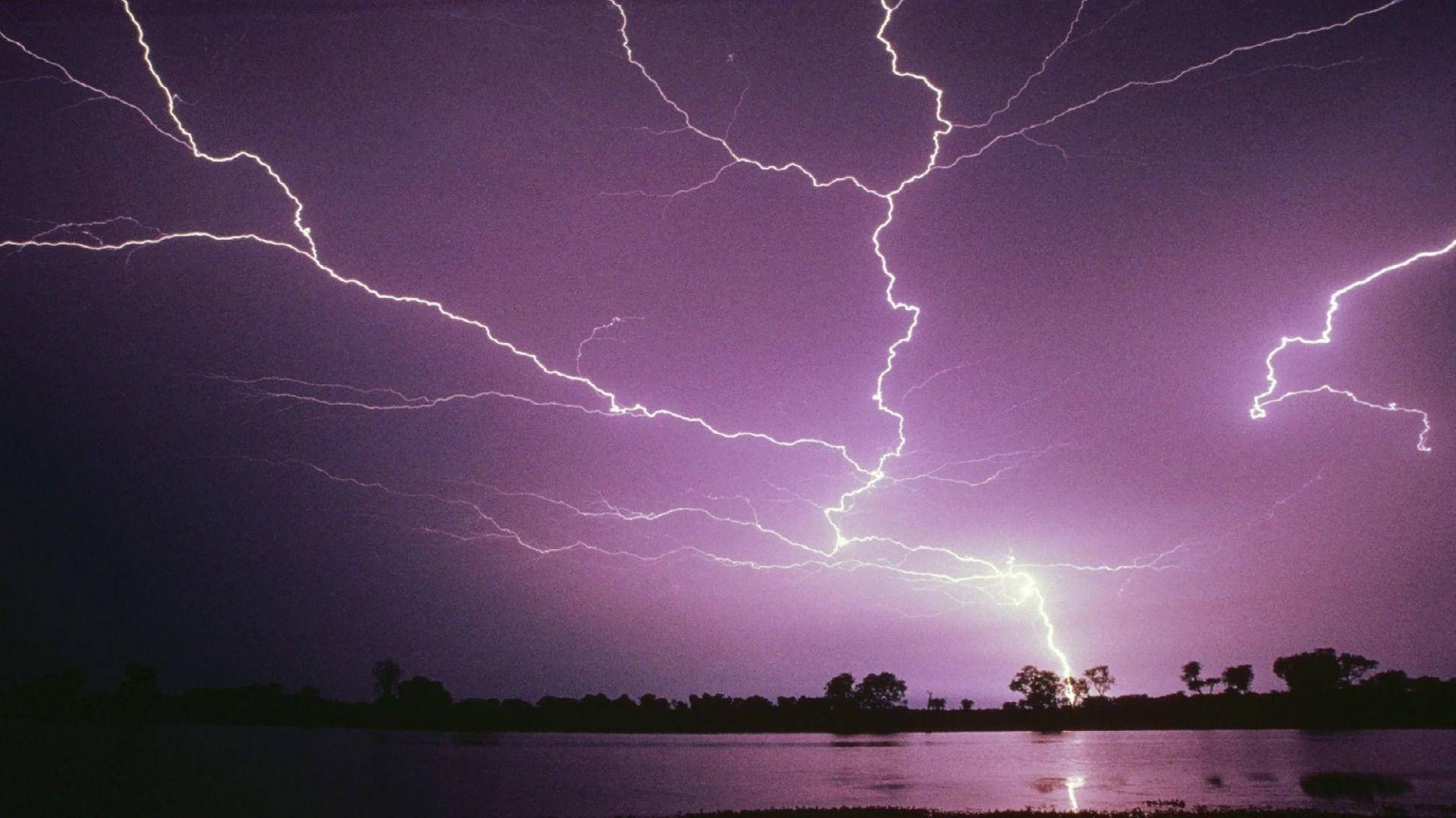 夜間黑暗湖面上方帶有閃電的紫色暴風雨天空