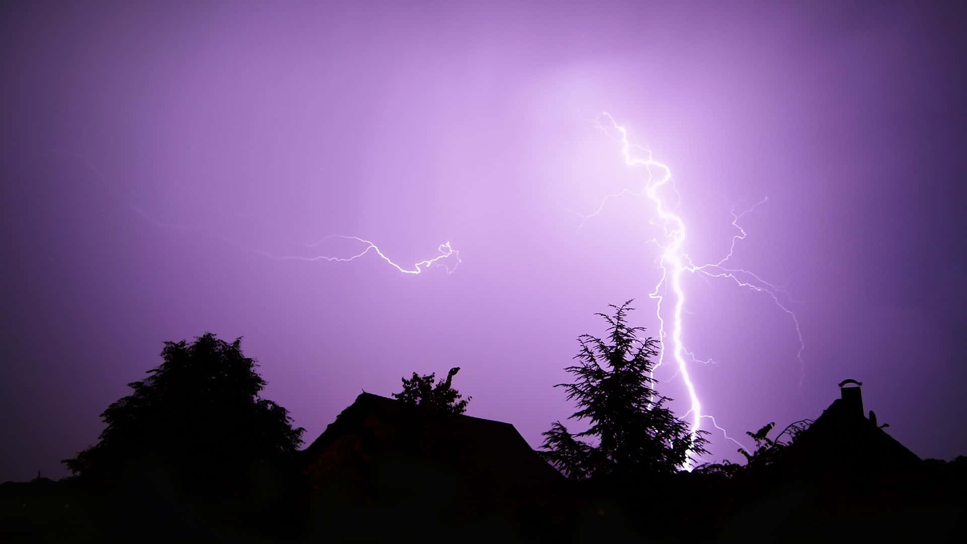 閃電擊中黑暗的屋頂和樹木，背景是紫羅蘭色的暴風雨天空。