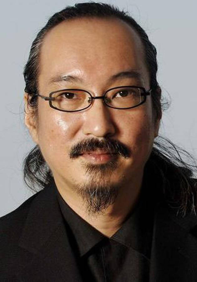 細川紘一的動畫宇宙 壁紙 — 一位戴眼鏡和鬍子的男士，身穿黑色西裝，背景為純灰色。