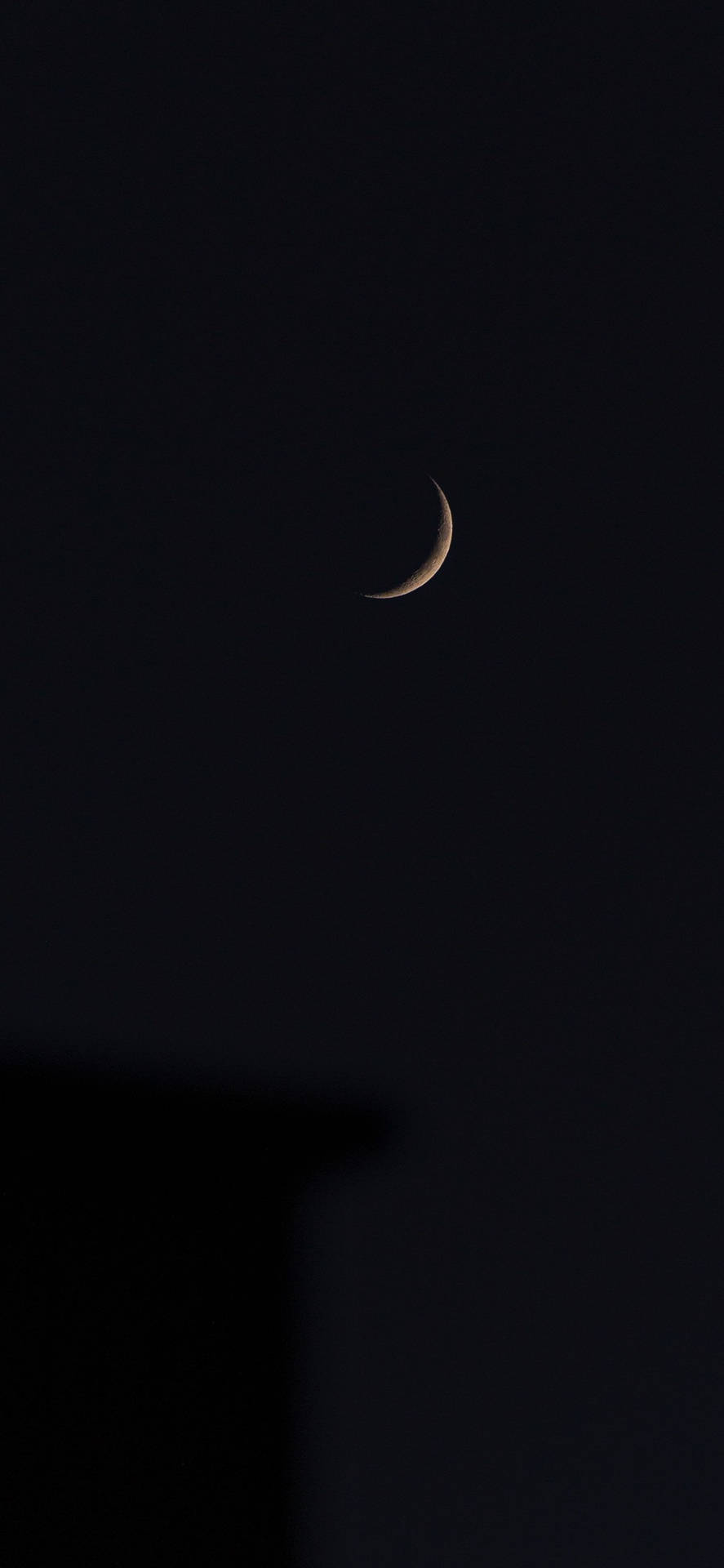 一彎月牙在黑暗的夜空中閃耀，位於建築物剪影之上。