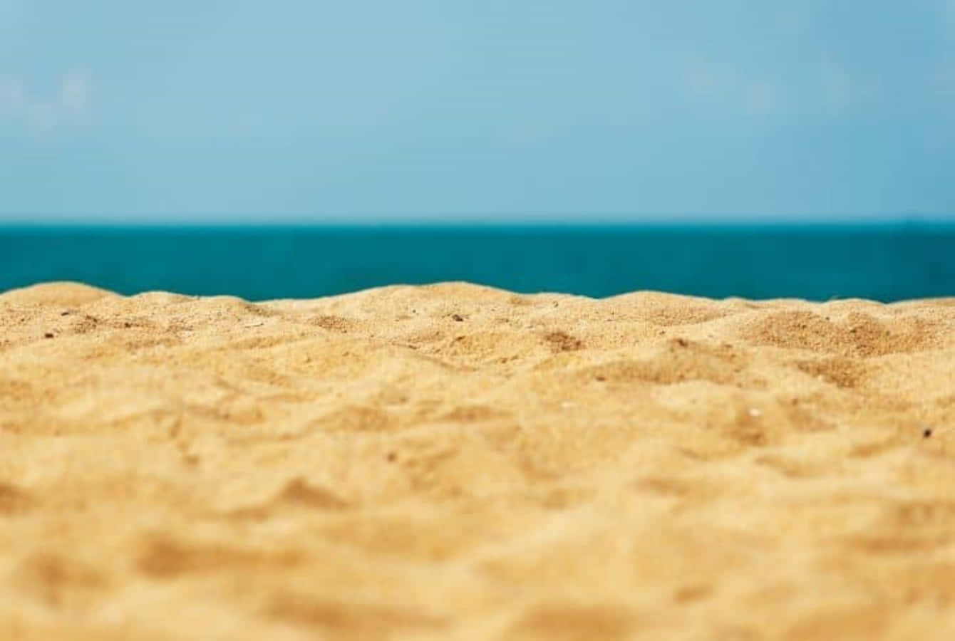 細沙海灘美景 壁紙 — 特寫鏡頭：紋理金黃色沙灘與碧綠海洋在清澈藍天下交匯。