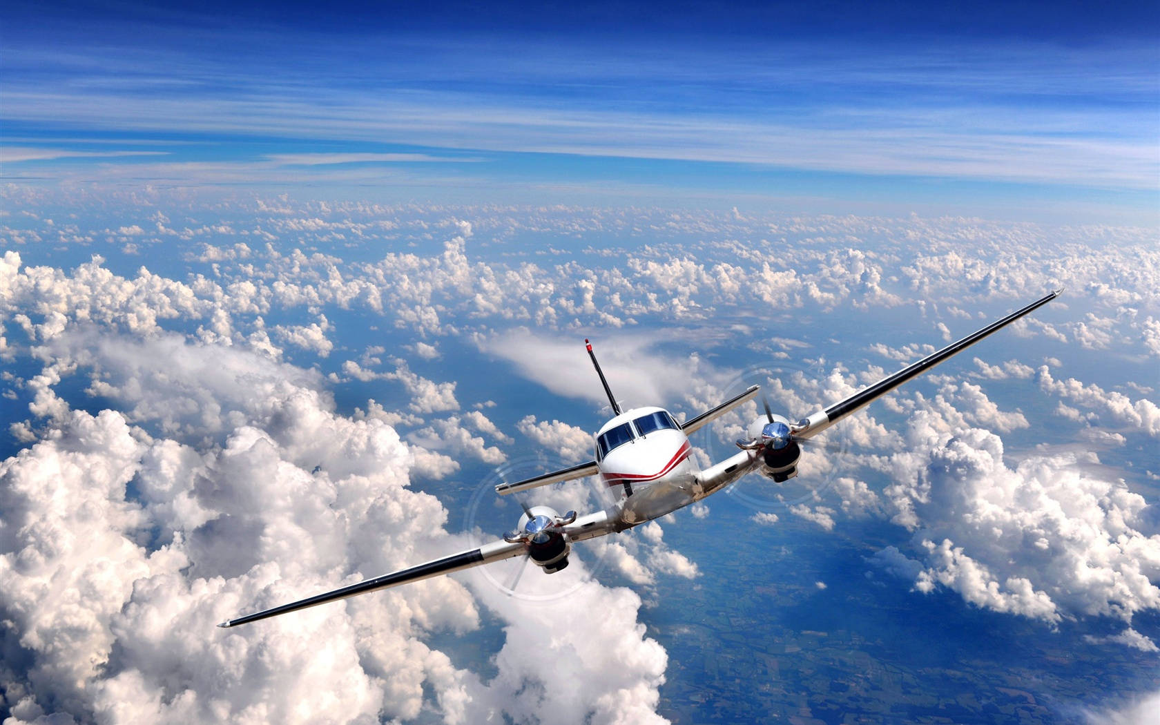 細長小型飛機高飛於雲海 壁紙 — 一架白色螺旋槳飛機在晴朗的藍天下翱翔於蓬鬆的白雲之上。