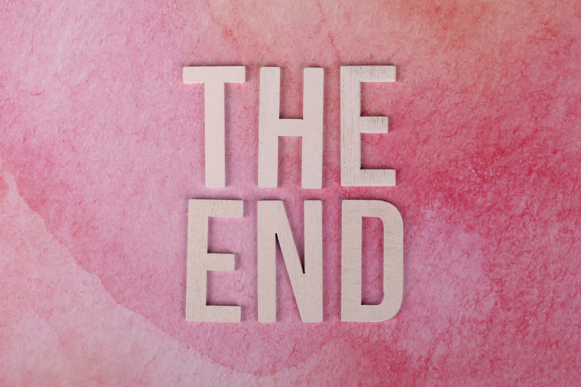 粉紅色水彩背景上拼出「THE END」的木製字母。
