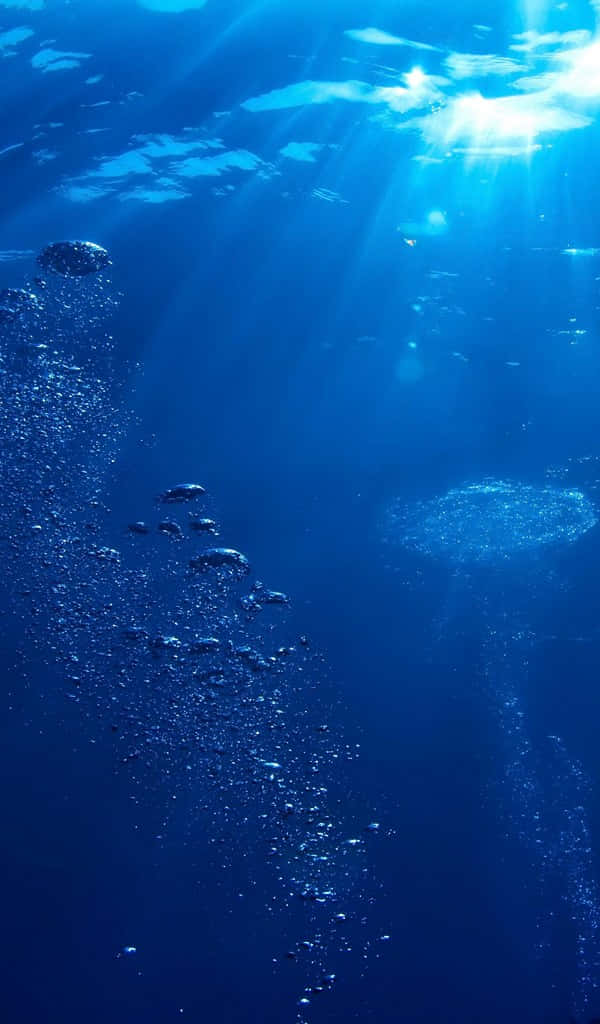 絢麗抽象瀑布 壁紙 — 陽光穿透深藍色海水，照亮下方旋轉的氣泡和漂浮的微粒。