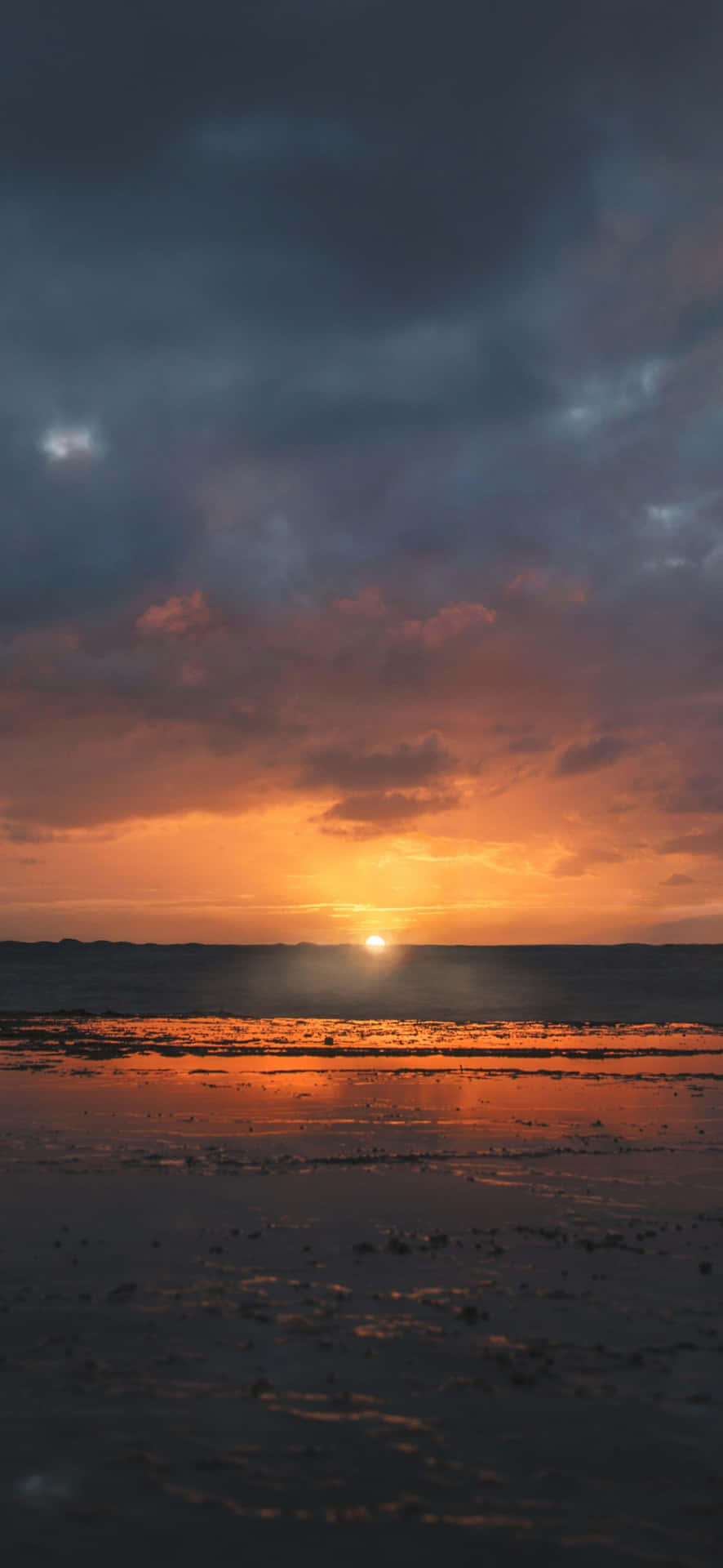 濕海灘上的日落，帶有橙色雲彩和黑暗天空