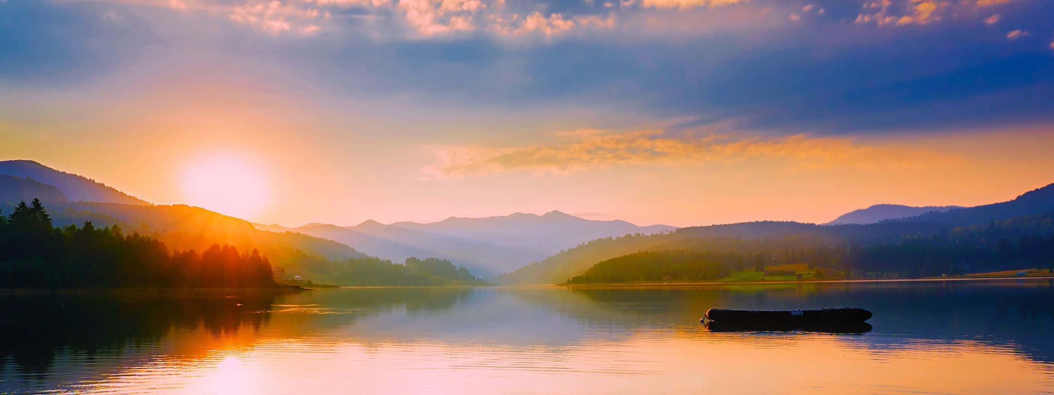 絢麗星夜極光 壁紙 — 夕陽將山脈和湖泊染成溫暖的金色和深藍色，一根孤獨的木頭靜靜地漂浮在平靜的水面上。