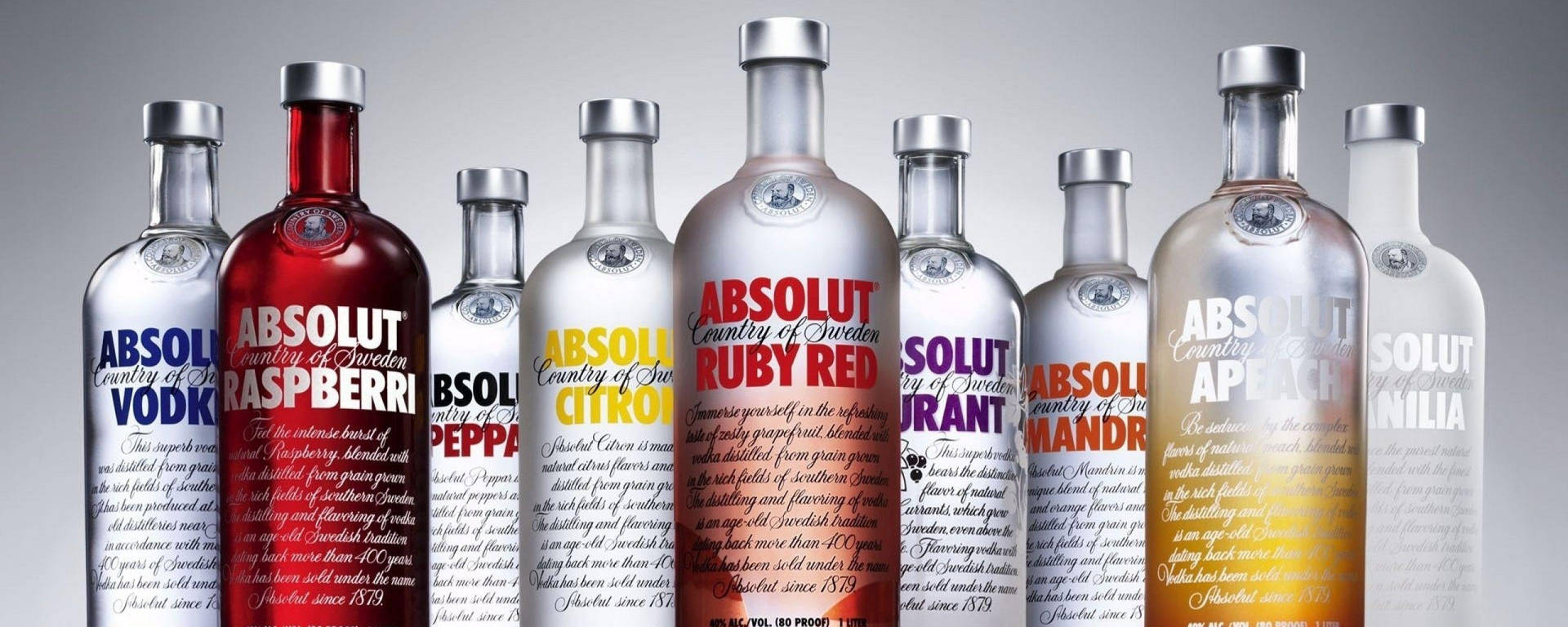 灰色背景上的一排不同口味Absolut伏特加酒瓶。