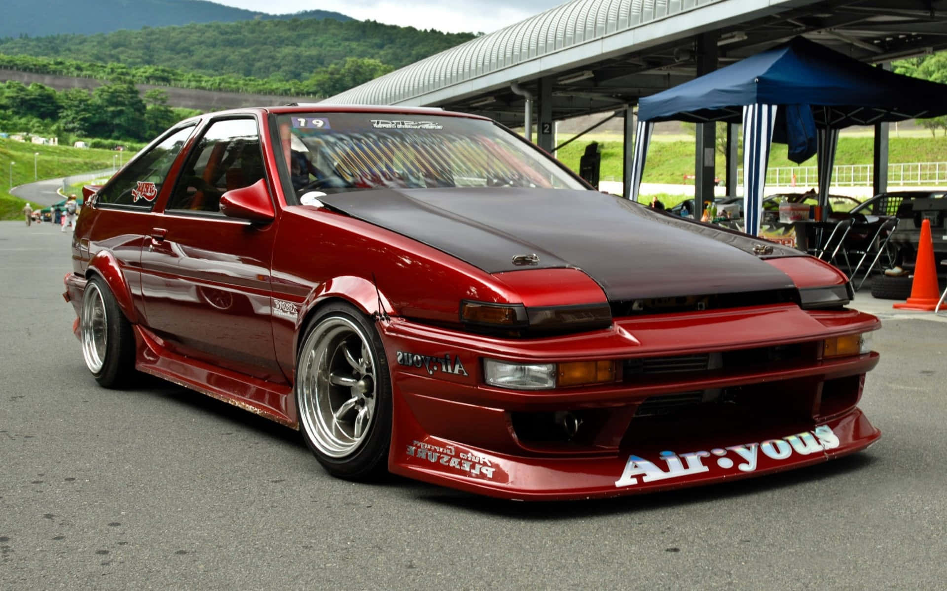 賽車場上的紅色改裝豐田AE86飄移車，背景有綠色山丘。