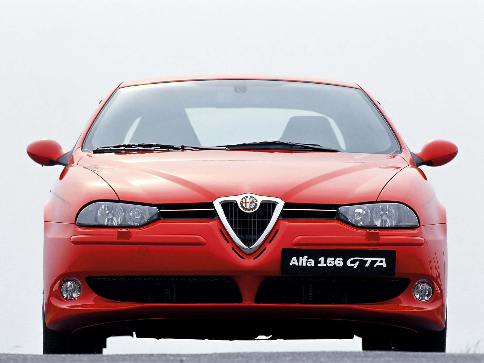 經典 Alfa Romeo 156 飛馳中 壁紙 — 一輛充滿活力的紅色Alfa 156 GTA跑車正面朝向純白色背景，展示其標誌性格柵和時尚車頭燈。