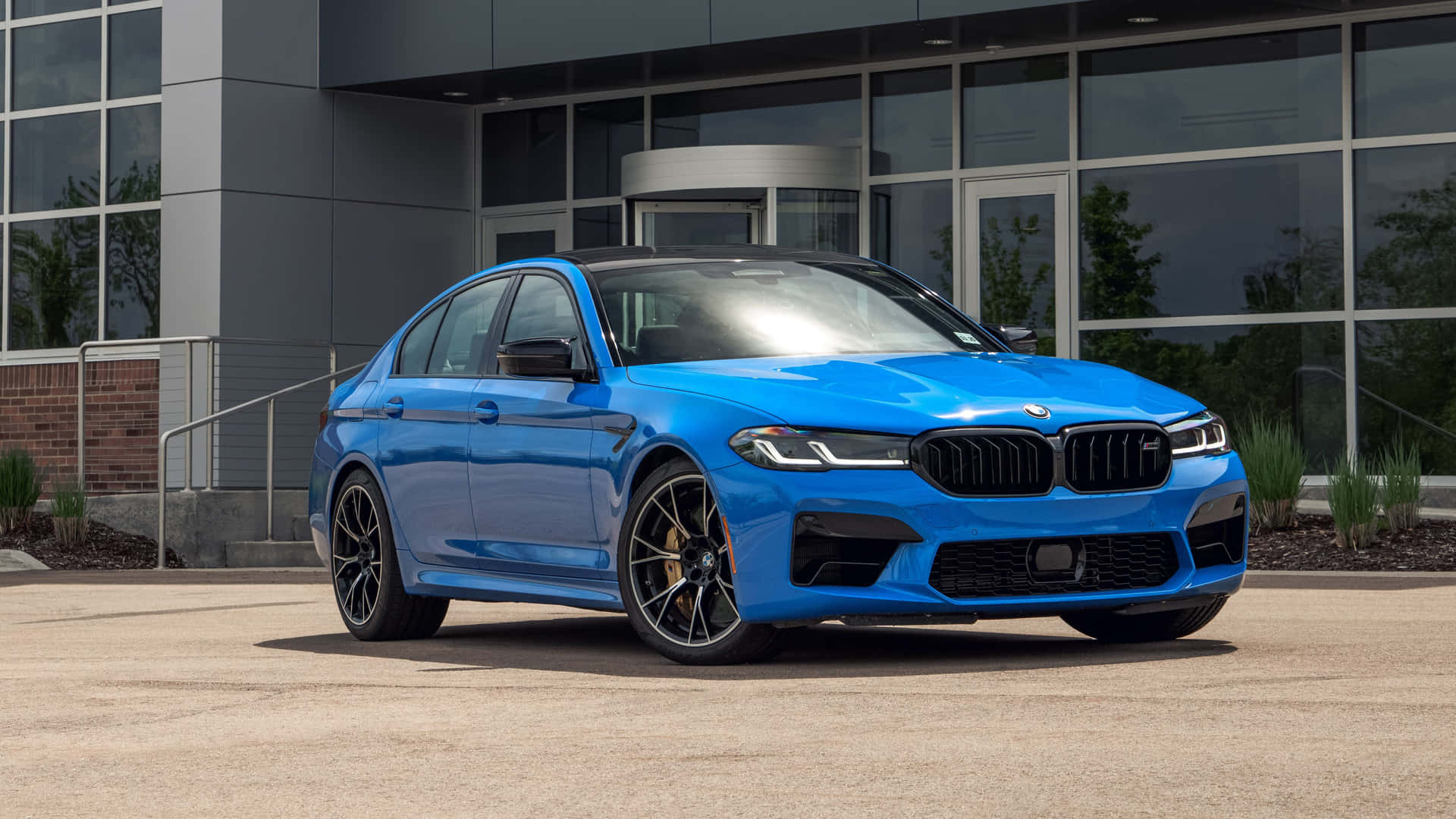 藍色BMW M5轎車停在現代辦公大樓前。