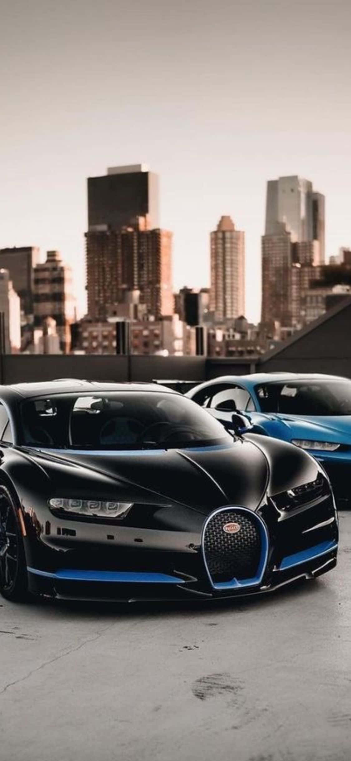 經典 Bugatti 與創新 iPhone Xs 完美協調 壁紙 — 兩輛時尚的Bugatti超跑停在屋頂上，城市天際線在溫暖的日落光芒中閃耀。