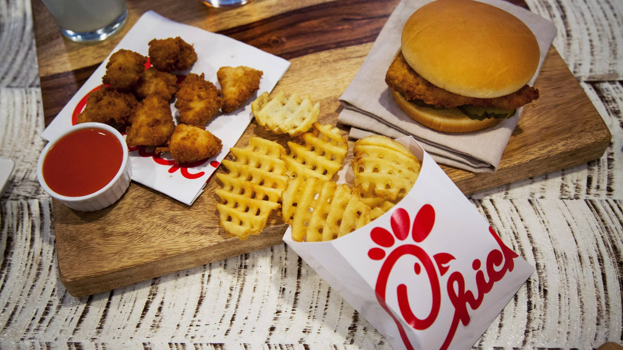 經典 Chick Fil A 餐點 壁紙 — 脆皮雞肉三文治、窩夫薯條及雞柳，盛載於木板上，附上蘸醬。