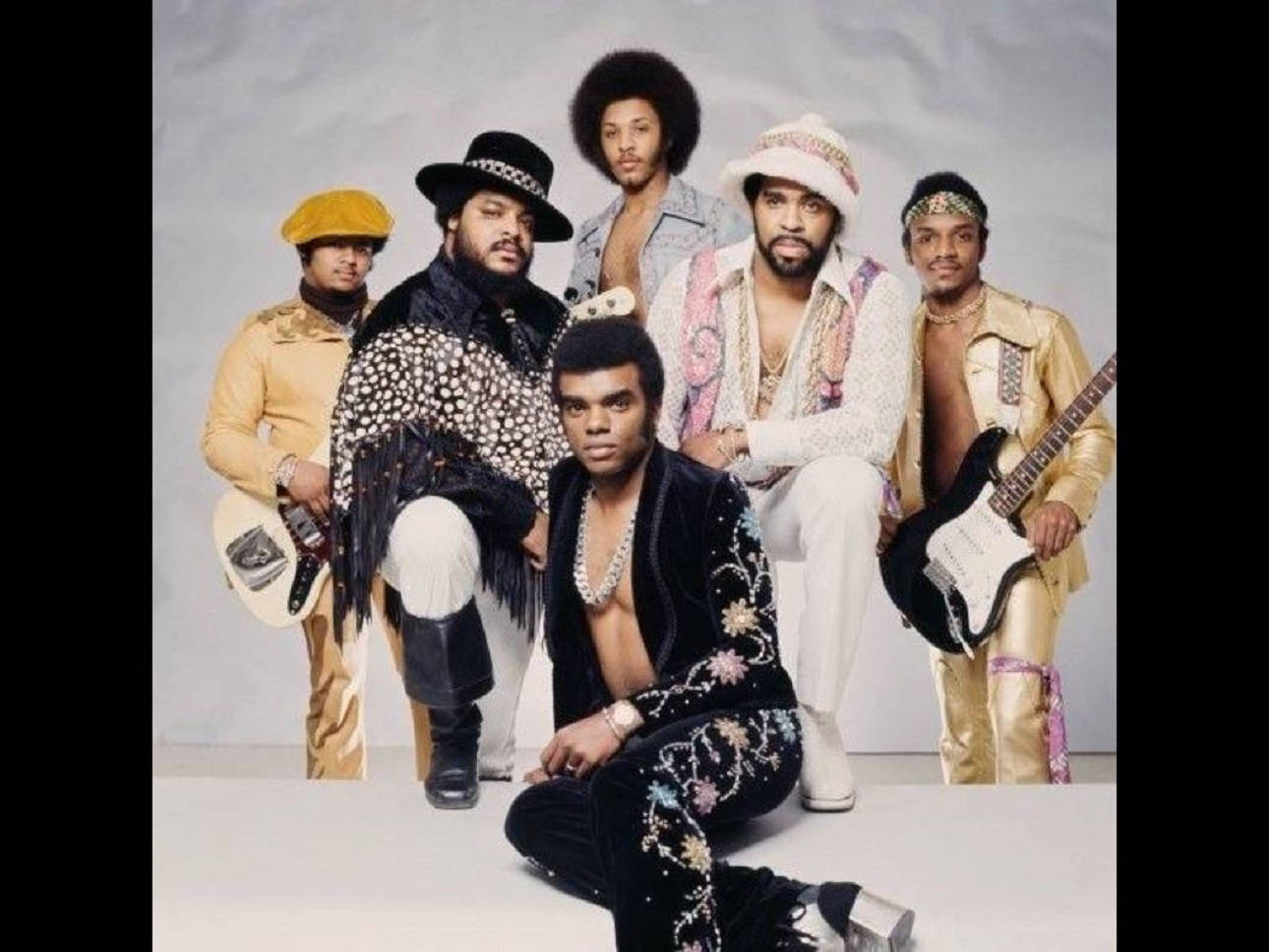 經典 Isley Brothers 專輯封面 壁紙 — 放克樂隊 Earth, Wind & Fire 的復古工作室肖像，穿著華麗的 1970 年代服裝，在中性背景前拿著結他擺姿勢。