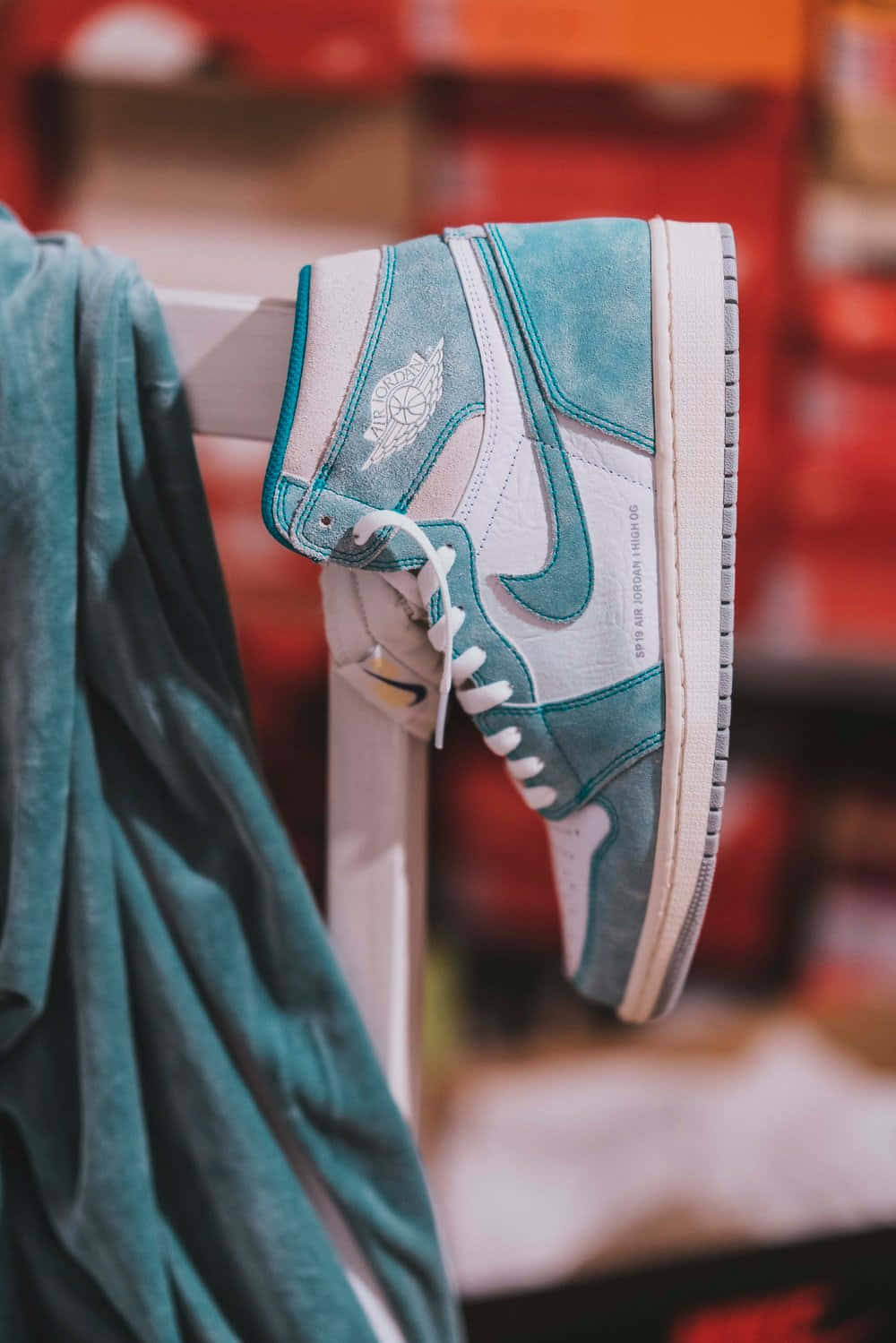 經典 Nike Air Jordan 壁紙 — 一隻青綠色和白色的高筒運動鞋掛在相配的青綠色連帽衫旁邊，背景是模糊的紅色。