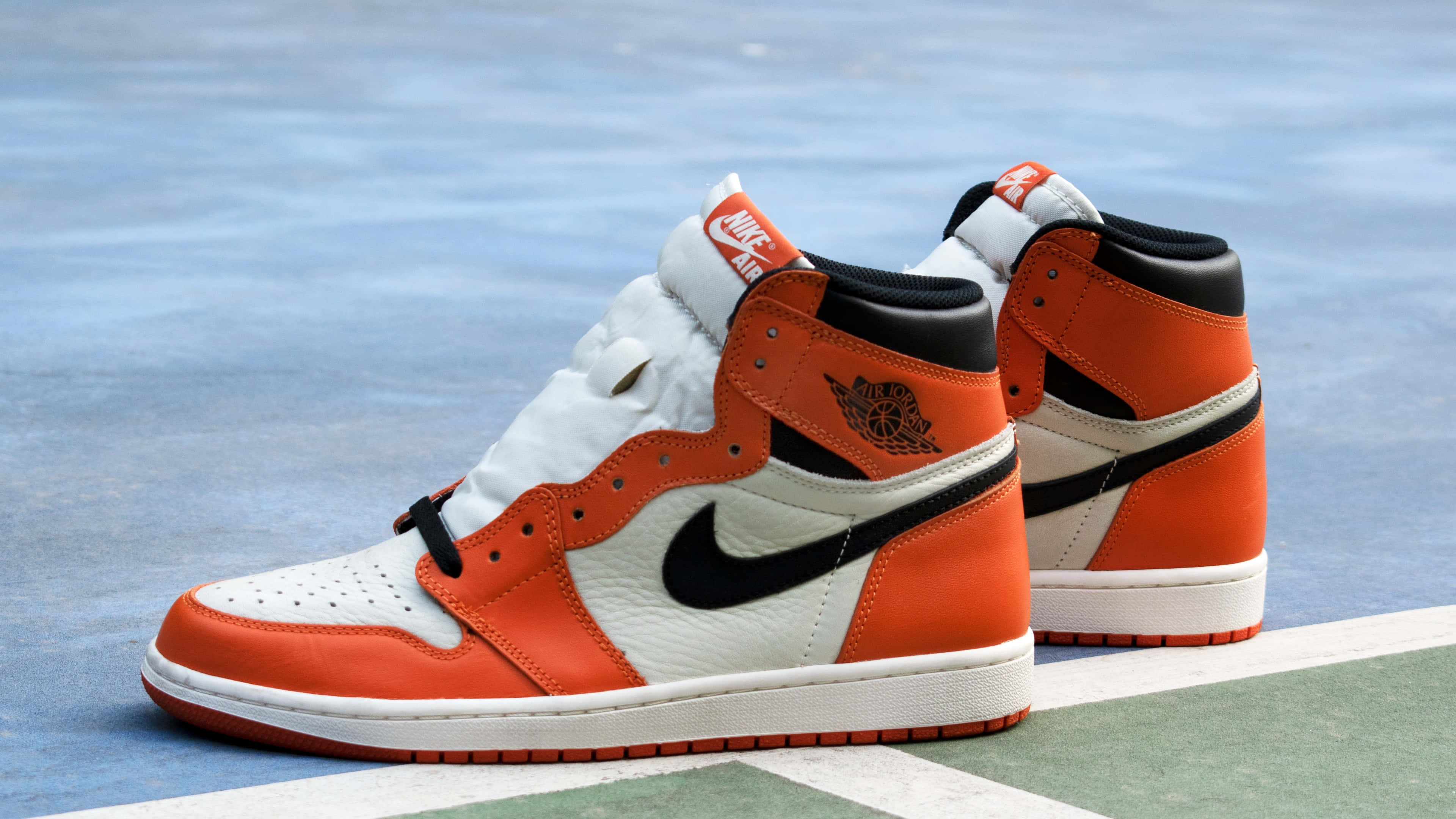 經典 Nike Air Jordan 鞋款，4K逼真壁紙 壁紙 — 鮮豔的橙色和白色 Air Jordan 1 運動鞋放在藍色和綠色的籃球場表面上。