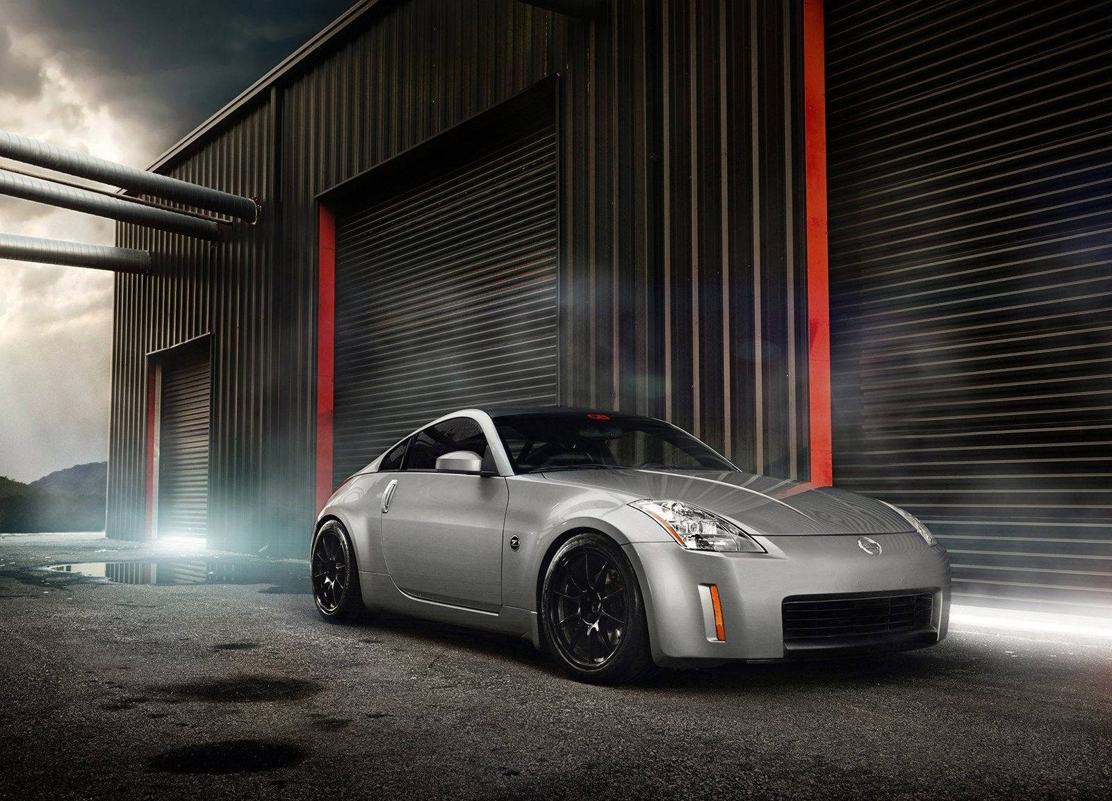 經典 Nissan 350z — 汽車藝術的傑作 壁紙 — 一輛時尚的銀色跑車在戲劇性燈光下閃耀，位於帶有紅色點綴的波紋金屬倉庫外。
