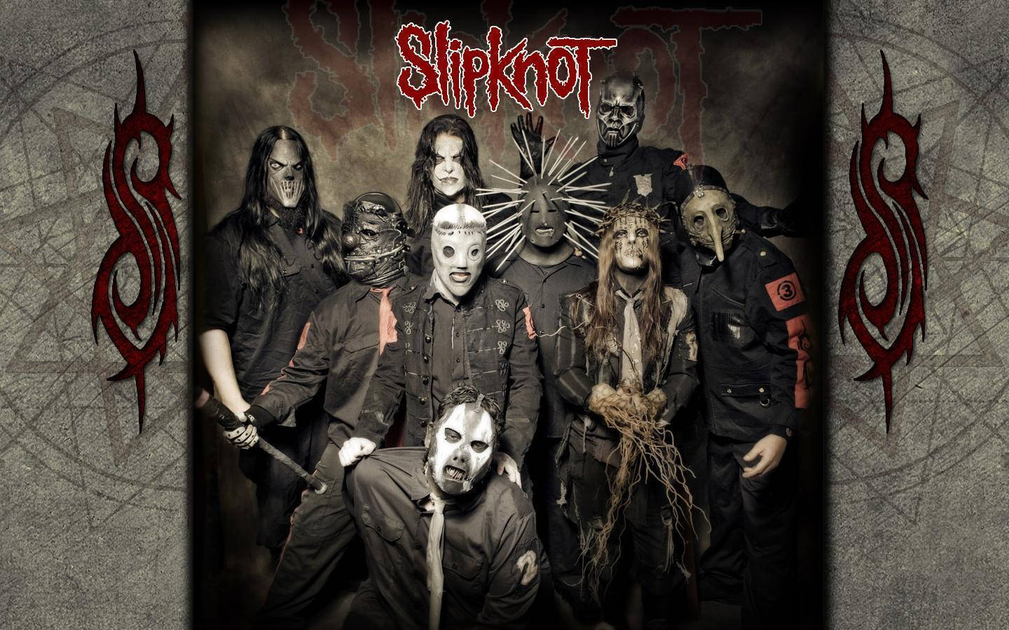 經典 Slipknot 專輯封面壁紙 壁紙 — Slipknot 樂團成員戴著怪誕面具，在帶有紅色部落標誌的破裂混凝土背景下強烈擺姿勢。