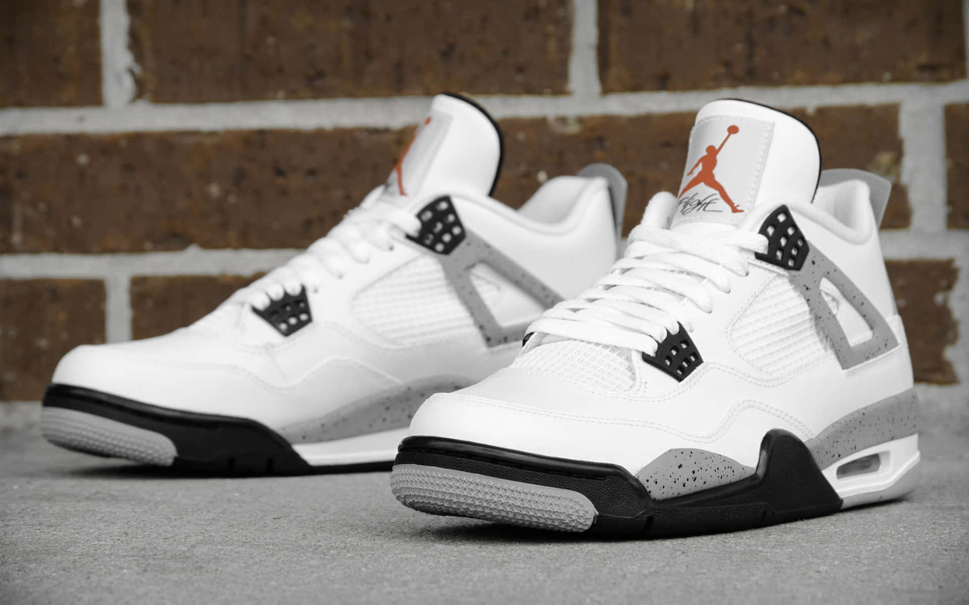 白色Jordan 4波鞋，黑色和橙色細節，背景為磚牆。