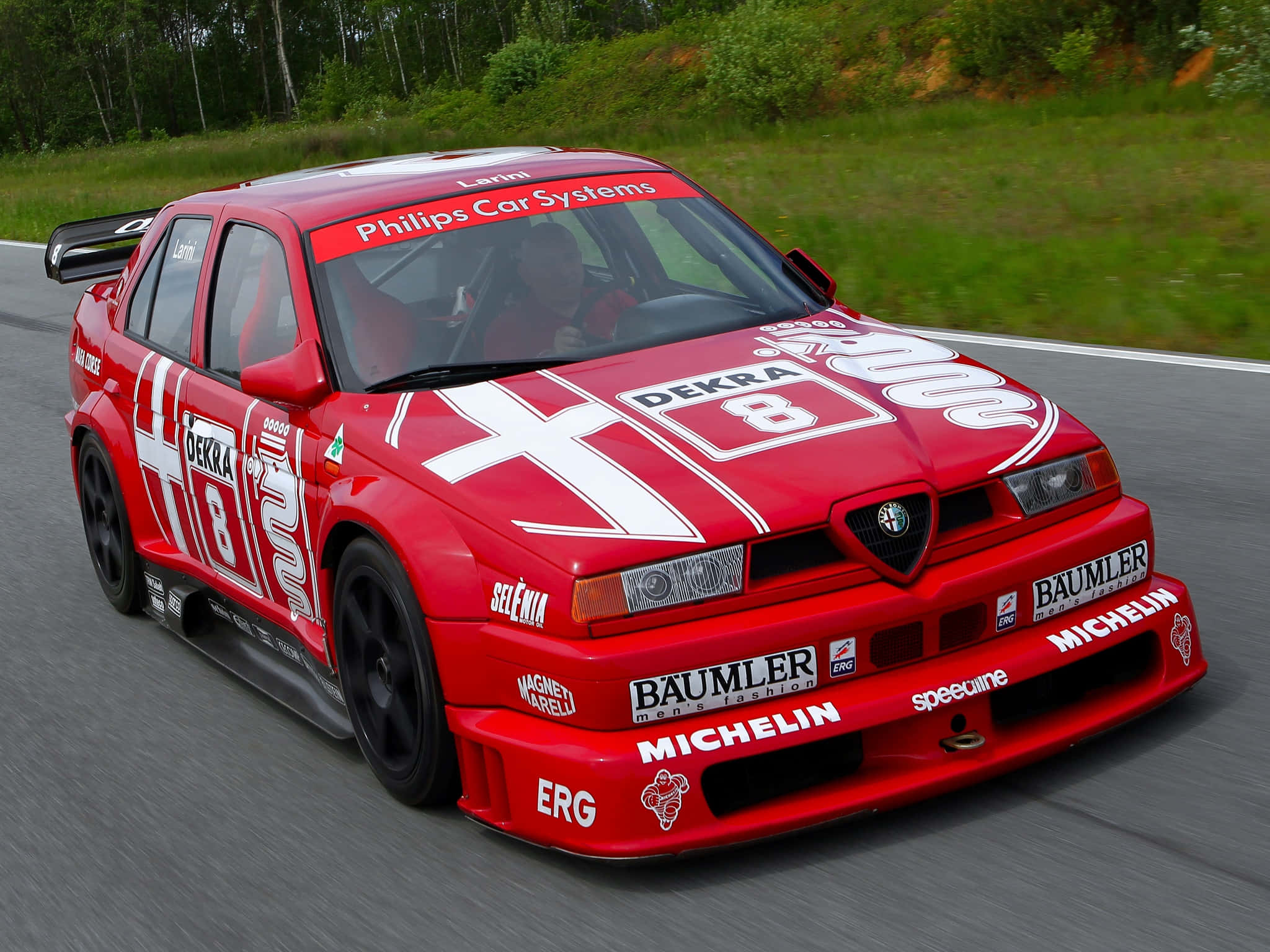 經典Alfa Romeo 壁紙 — 一輛帶有白色貼紙的紅色愛快羅密歐賽車沿著蜿蜒的道路疾馳，周圍環繞著綠樹和草地。