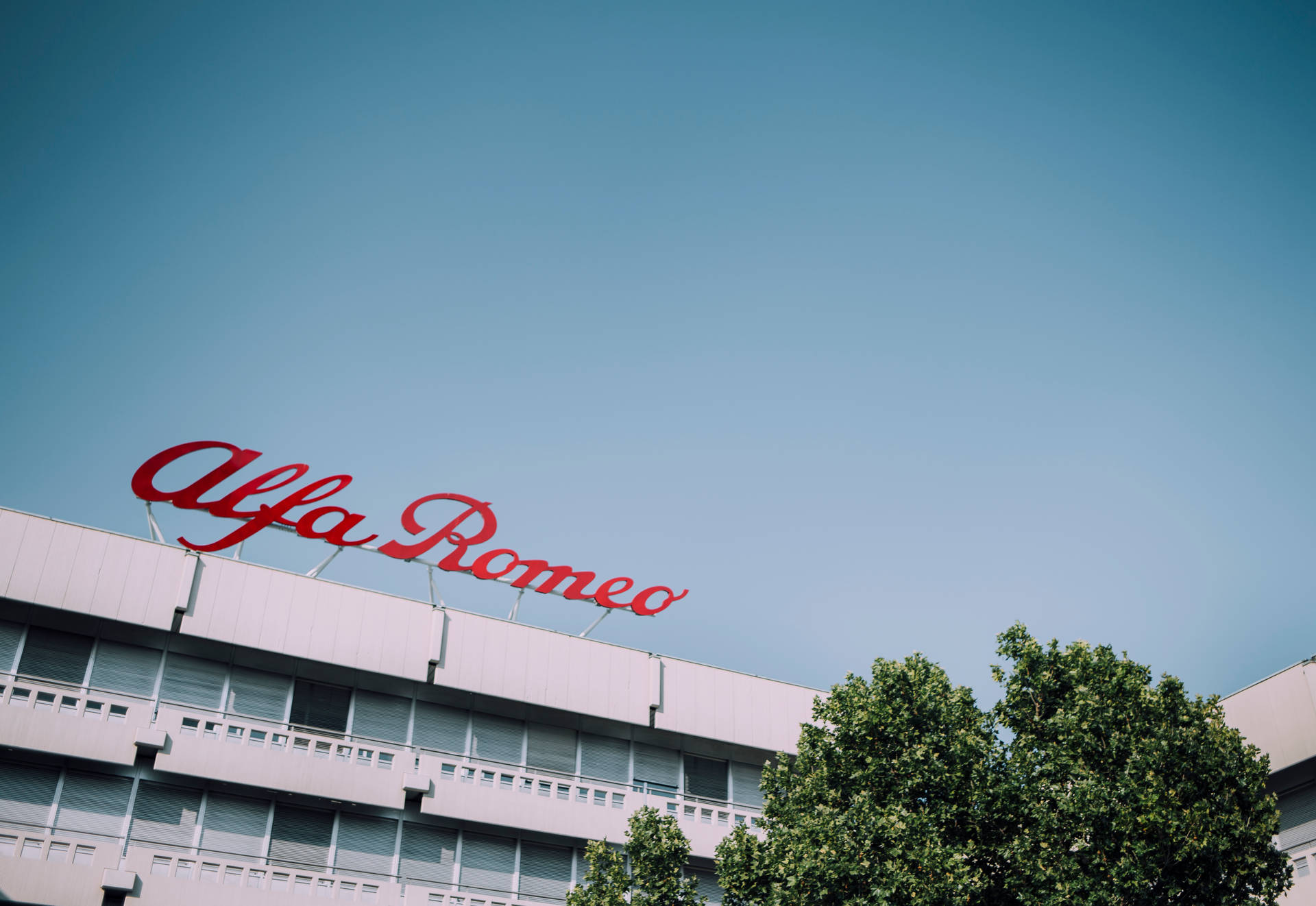 現代建築頂部的 Alfa Romeo 標誌，伴隨著樹木和藍天。