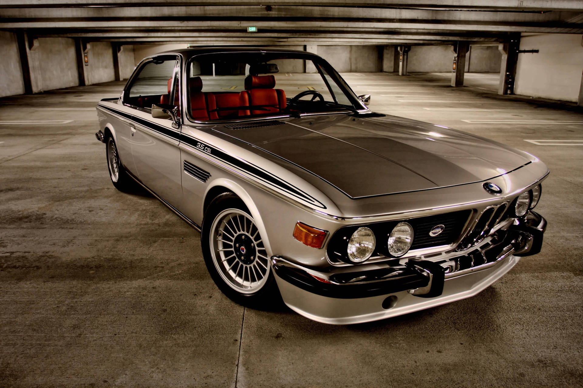 銀色復古BMW 3.0 CSL配紅色座椅停泊在空無一人的混凝土停車場。