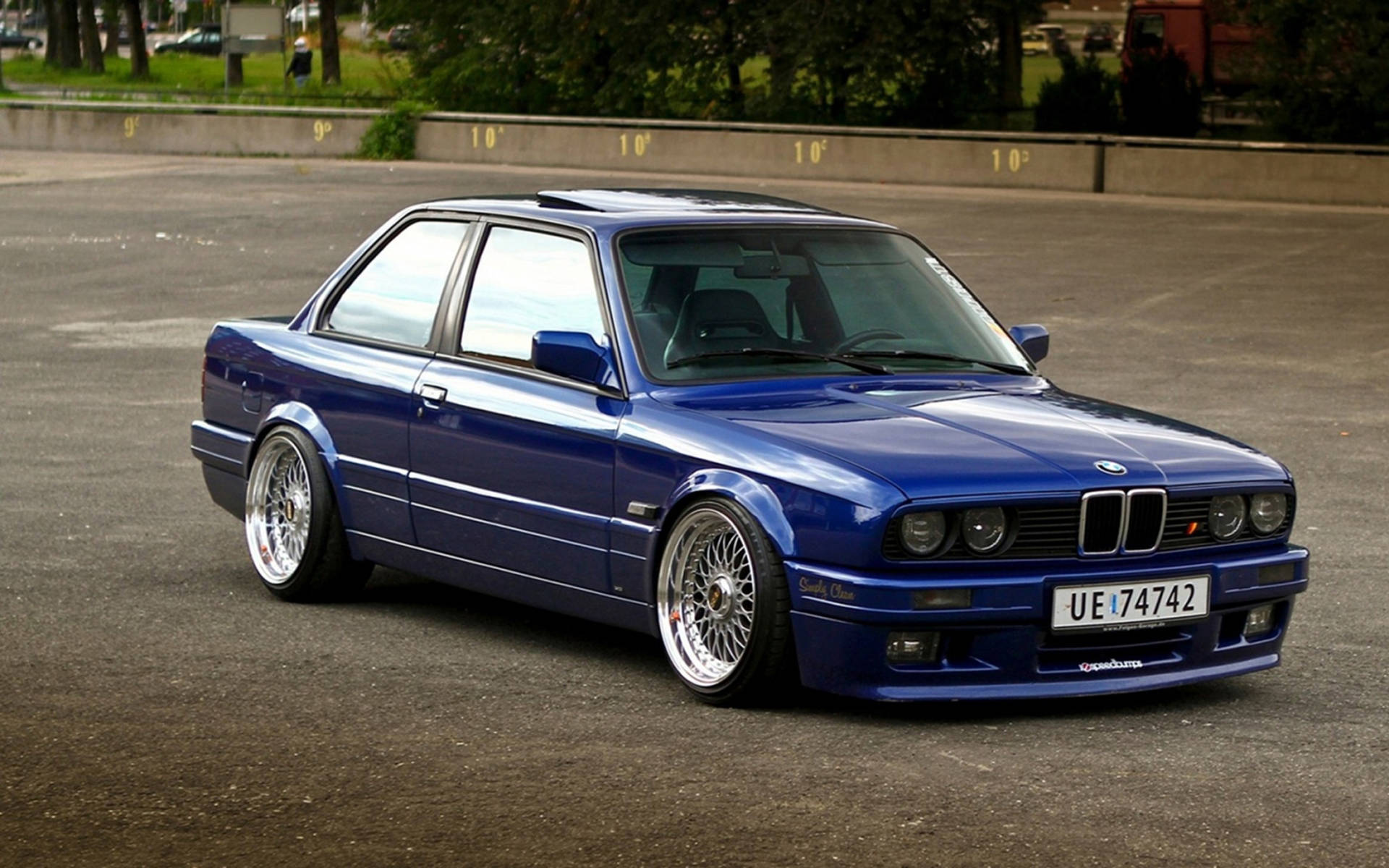 藍色BMW E30雙門轎跑車，降低懸掛並配備定制輪圈，停在瀝青路面上。