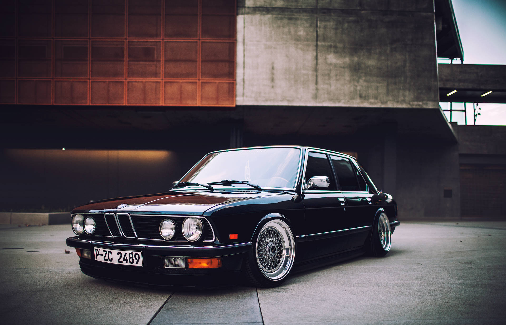 黑色經典BMW轎車配備定制輪圈，停在現代混凝土建築物前。