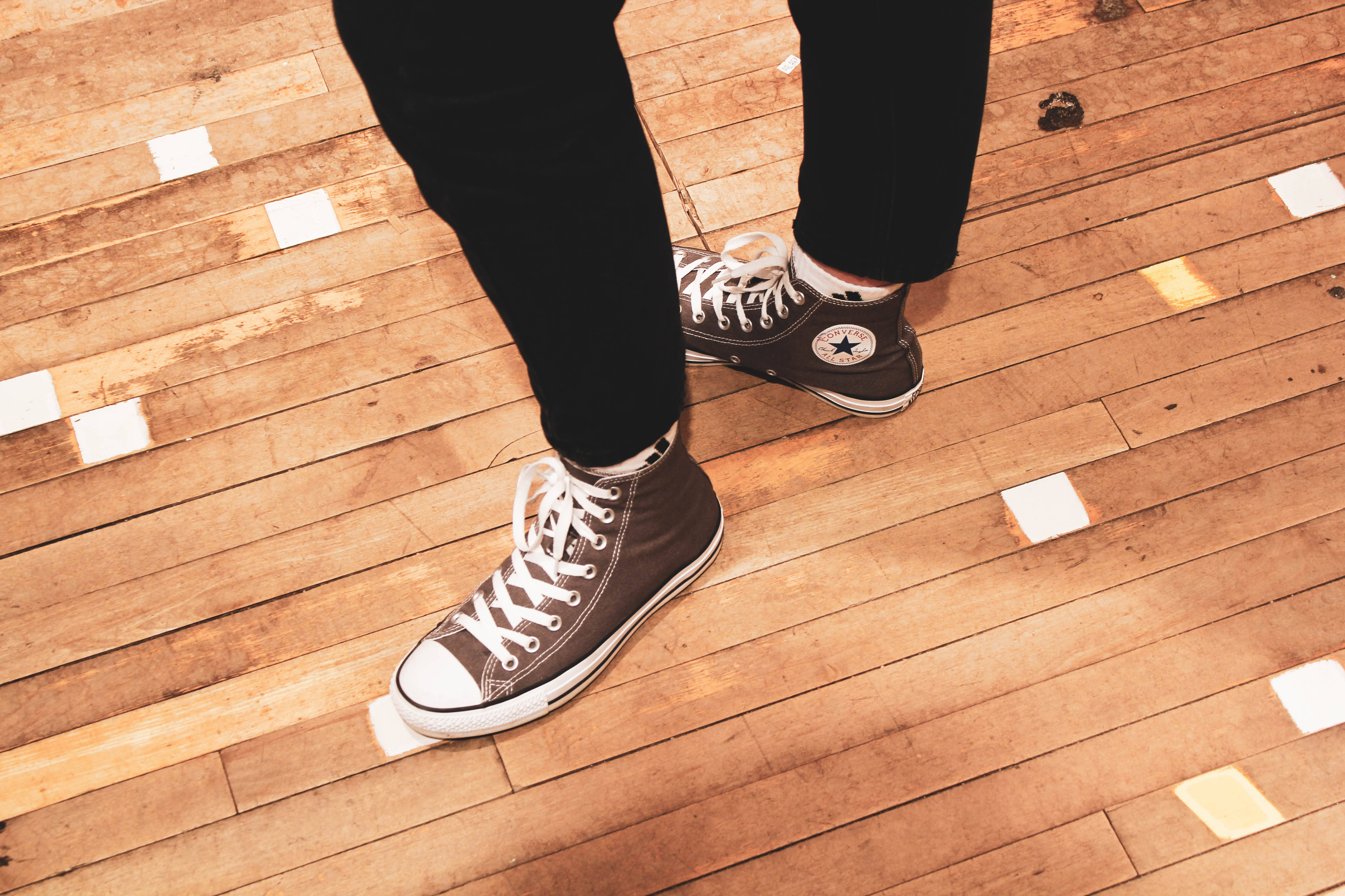 經典Converse All Star運動鞋 壁紙 — 棕色高筒運動鞋特寫，白色鞋帶和星星標誌，放在磨損的木地板上，散落著白色斑點。