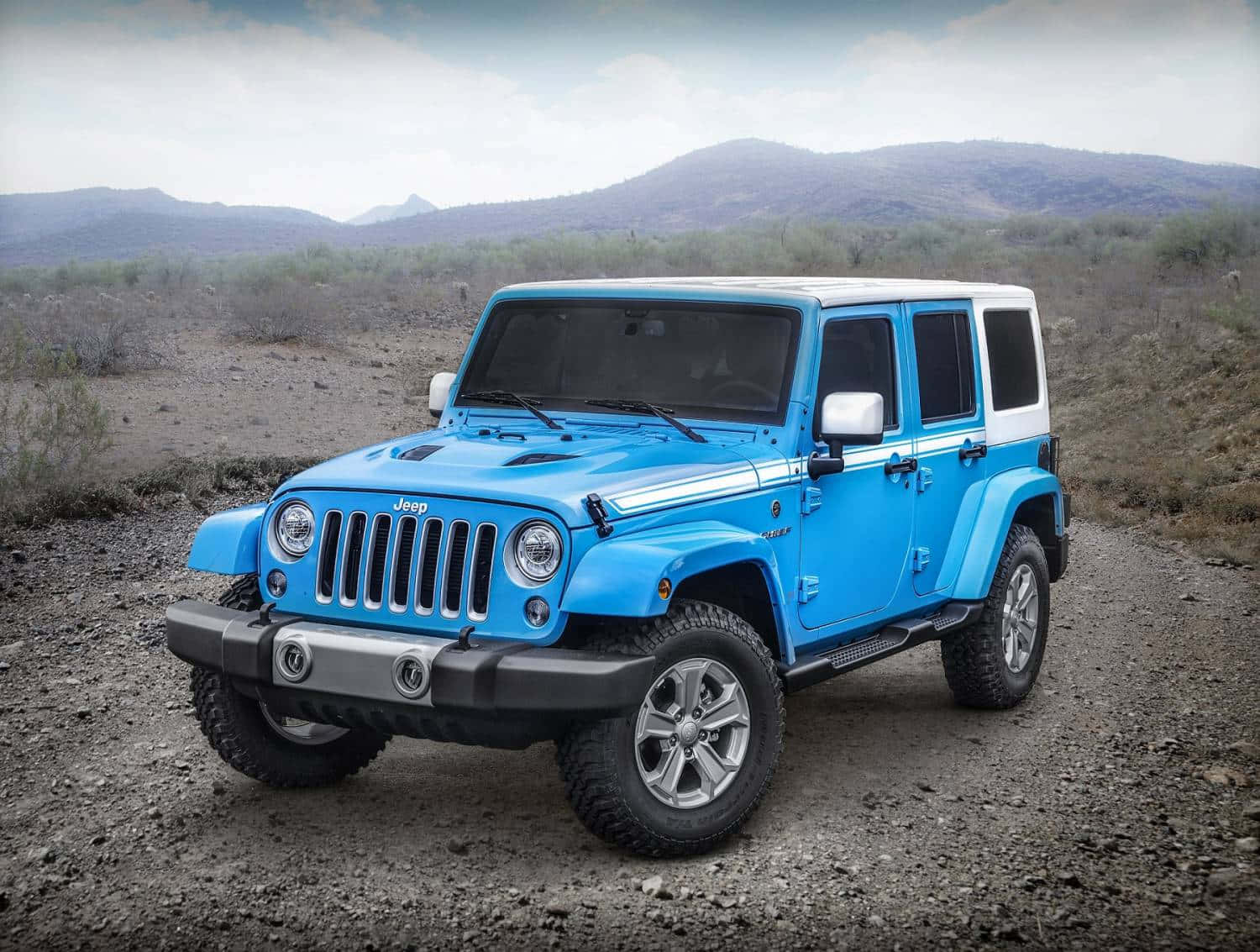 經典Jeep Wrangler — 你所需的全部動力 壁紙 — 一輛充滿活力的藍色Jeep Wrangler，白色車頂，停泊在乾燥山區沙漠景觀的碎石路上。