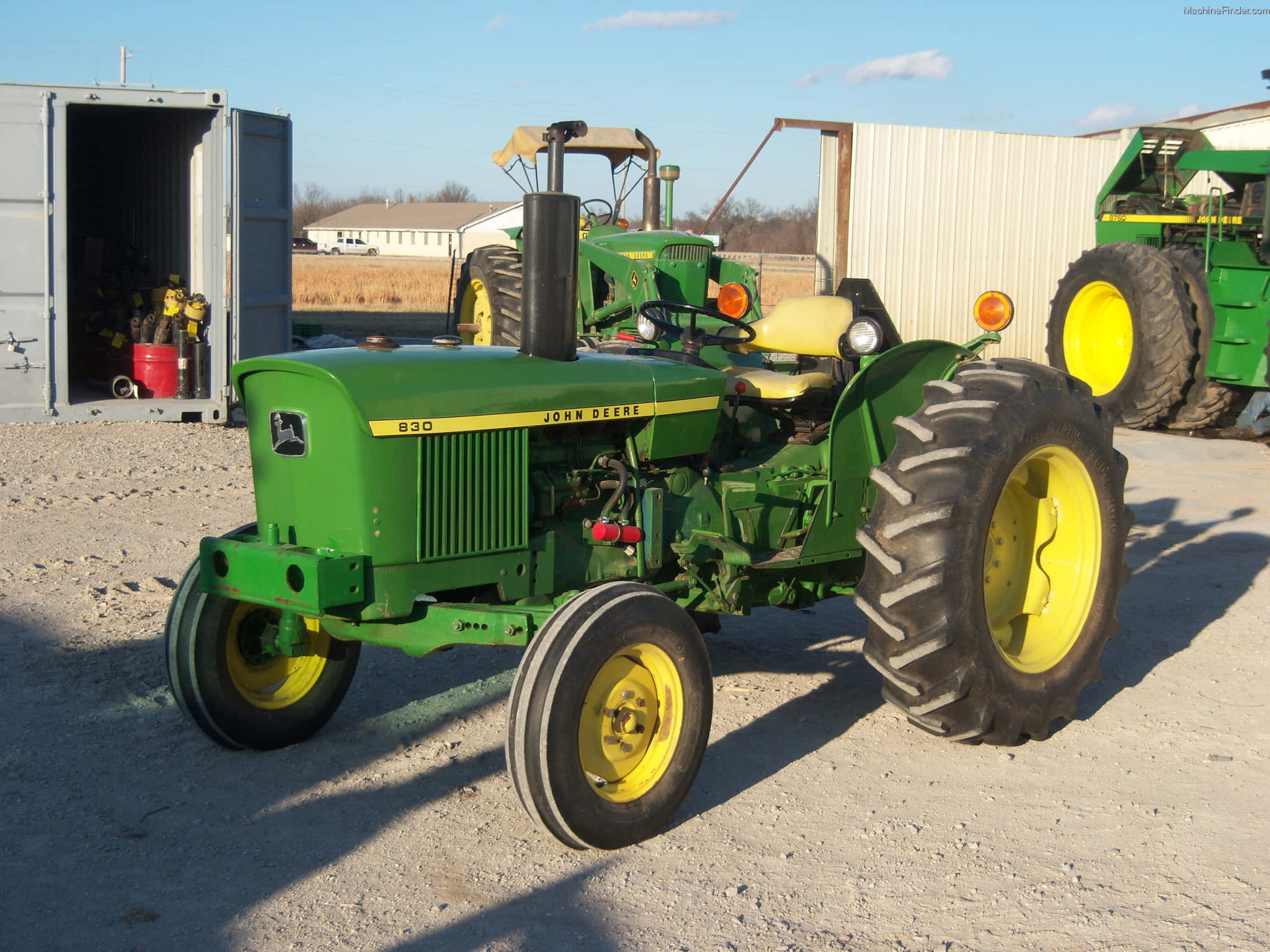 經典John Deere拖拉機 壁紙 — 一部復古綠色John Deere 830拖拉機帶黃色輪子，在明亮的陽光下停放在農場建築附近的礫石地上。
