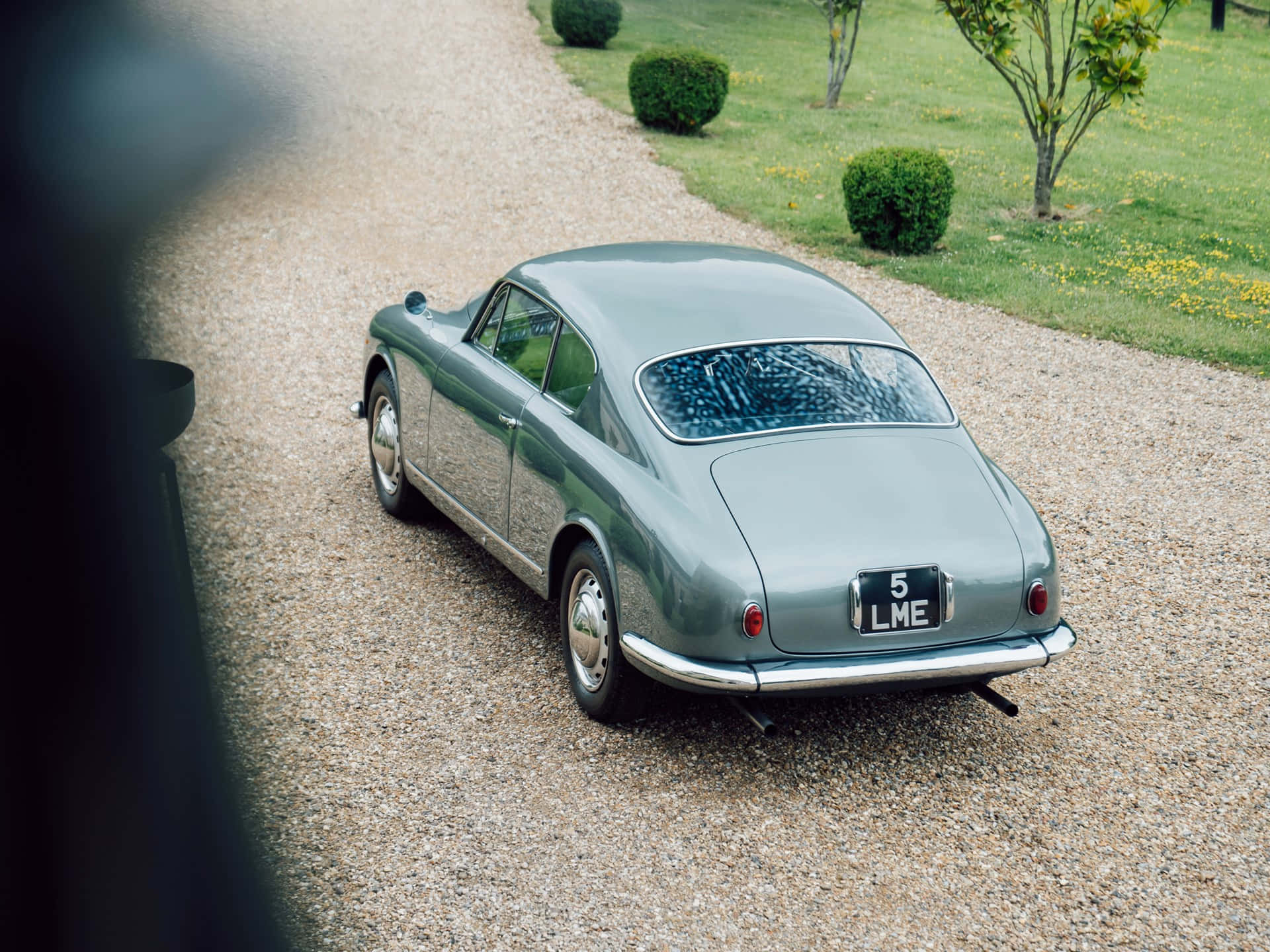 經典Lancia Aurelia B20 GT停泊 壁紙 — 一架時尚的復古綠色跑車停泊在碎石車道上，旁邊是修剪整齊的草坪和灌木叢。