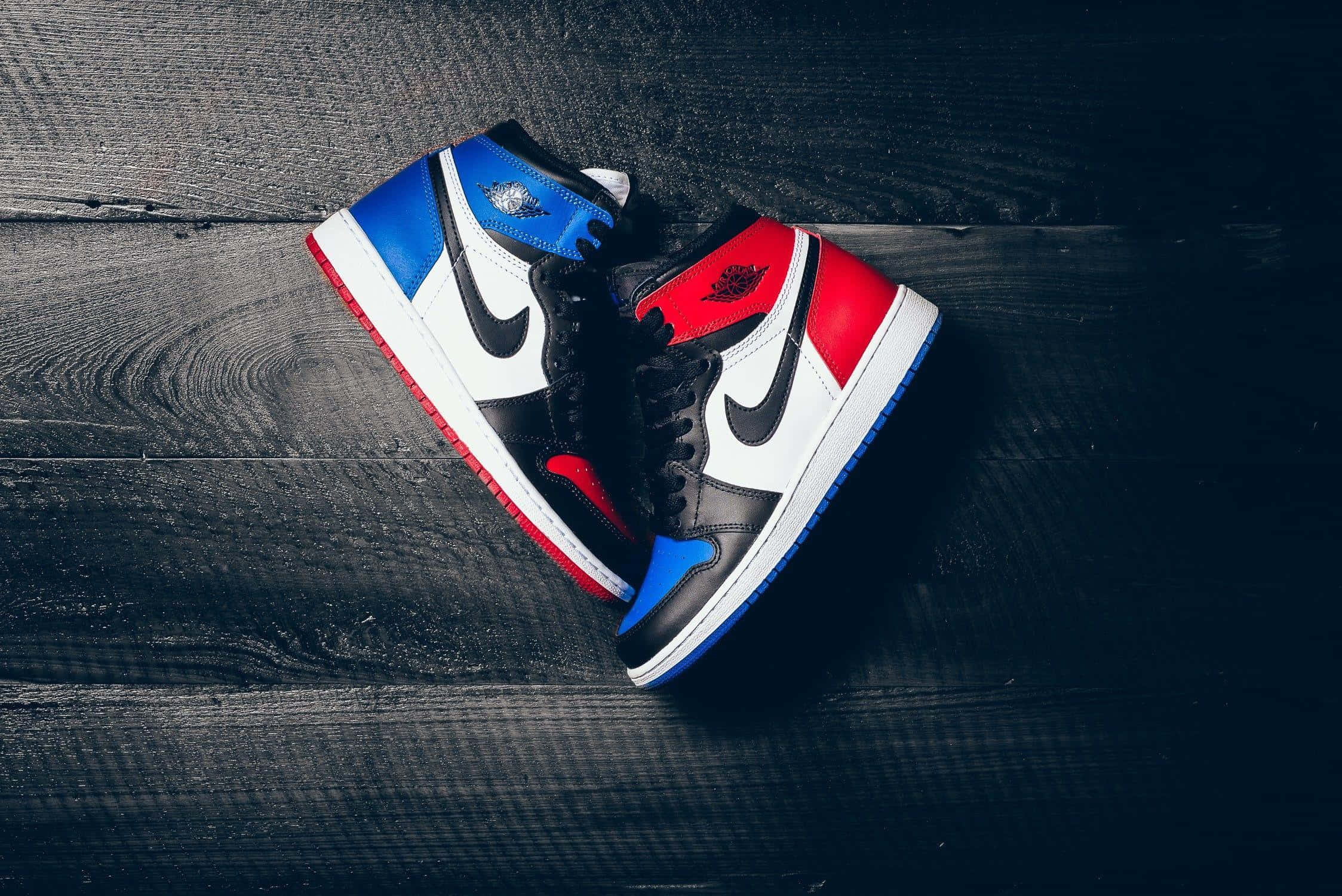 經典Nike Air Jordan運動鞋 壁紙 — 一對紅、藍、黑色 Jordan 1 運動鞋放在深色紋理木板上，配以戲劇性燈光。