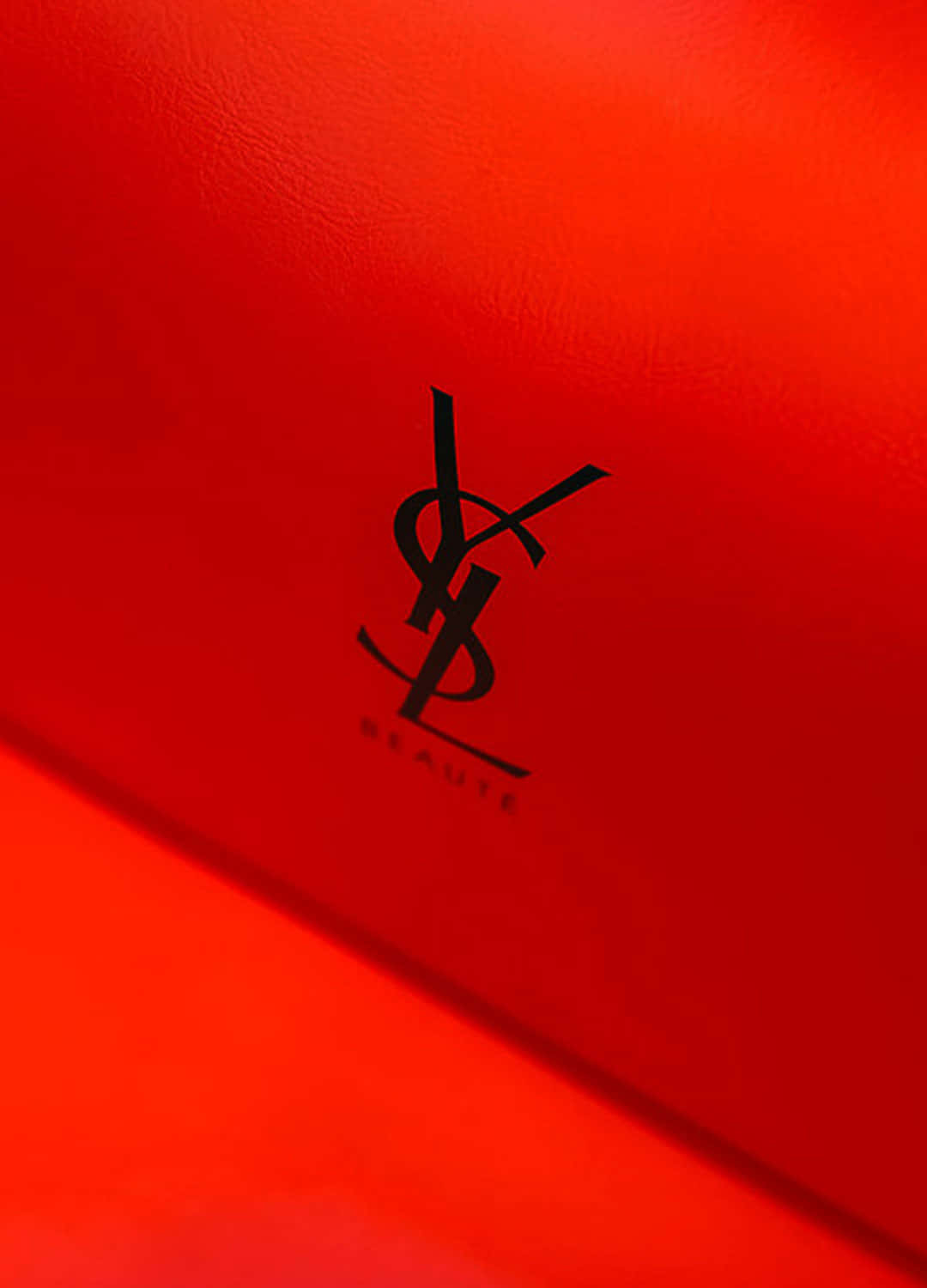 經典Yves Saint Laurent標誌，締造時尚史 壁紙 — 柔和燈光下，在質感豐富的紅色表面上特寫一個大膽的黑色YSL Beauté標誌。