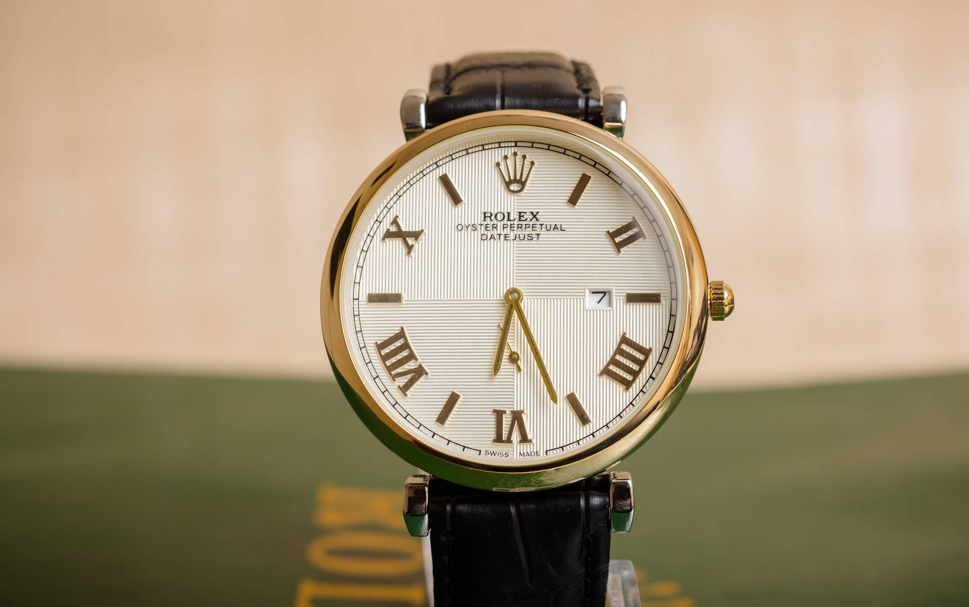 經典勞力士腕錶與地球模型：永恆奢華 壁紙 — 金色勞力士Oyster Perpetual Datejust手錶配黑色皮革錶帶的特寫，背景為模糊的米色和綠色。